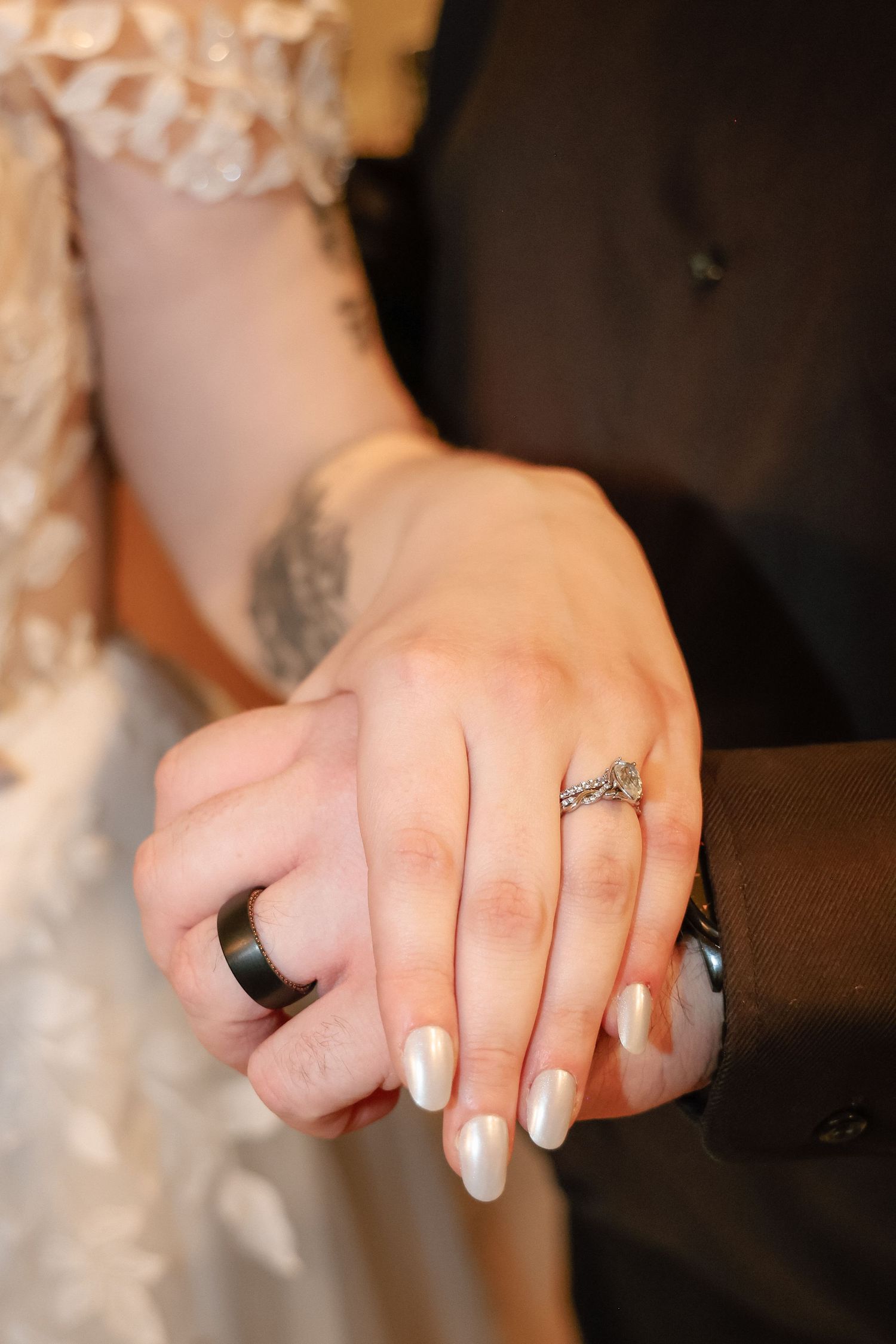 Newlyweds display their wedding rings, bride wearing diamond band with pearl nails, groom wearing black ring.