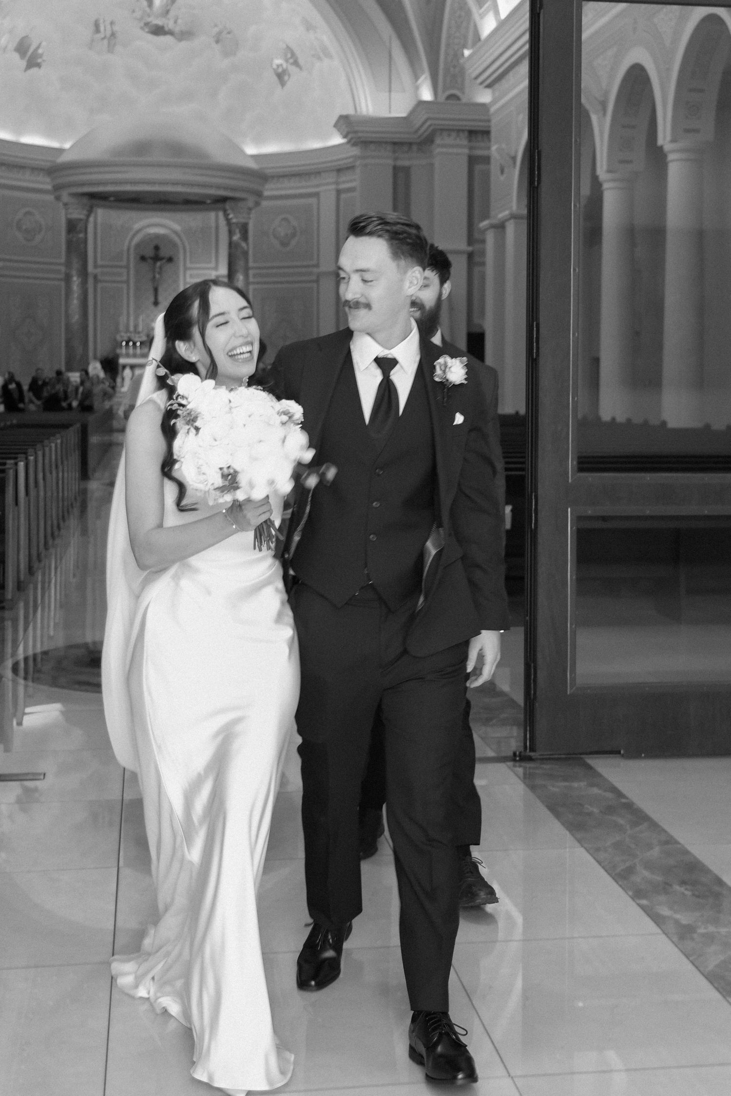 Black and white photo of a joyful bride and groom walking down the aisle after their church wedding ceremony.