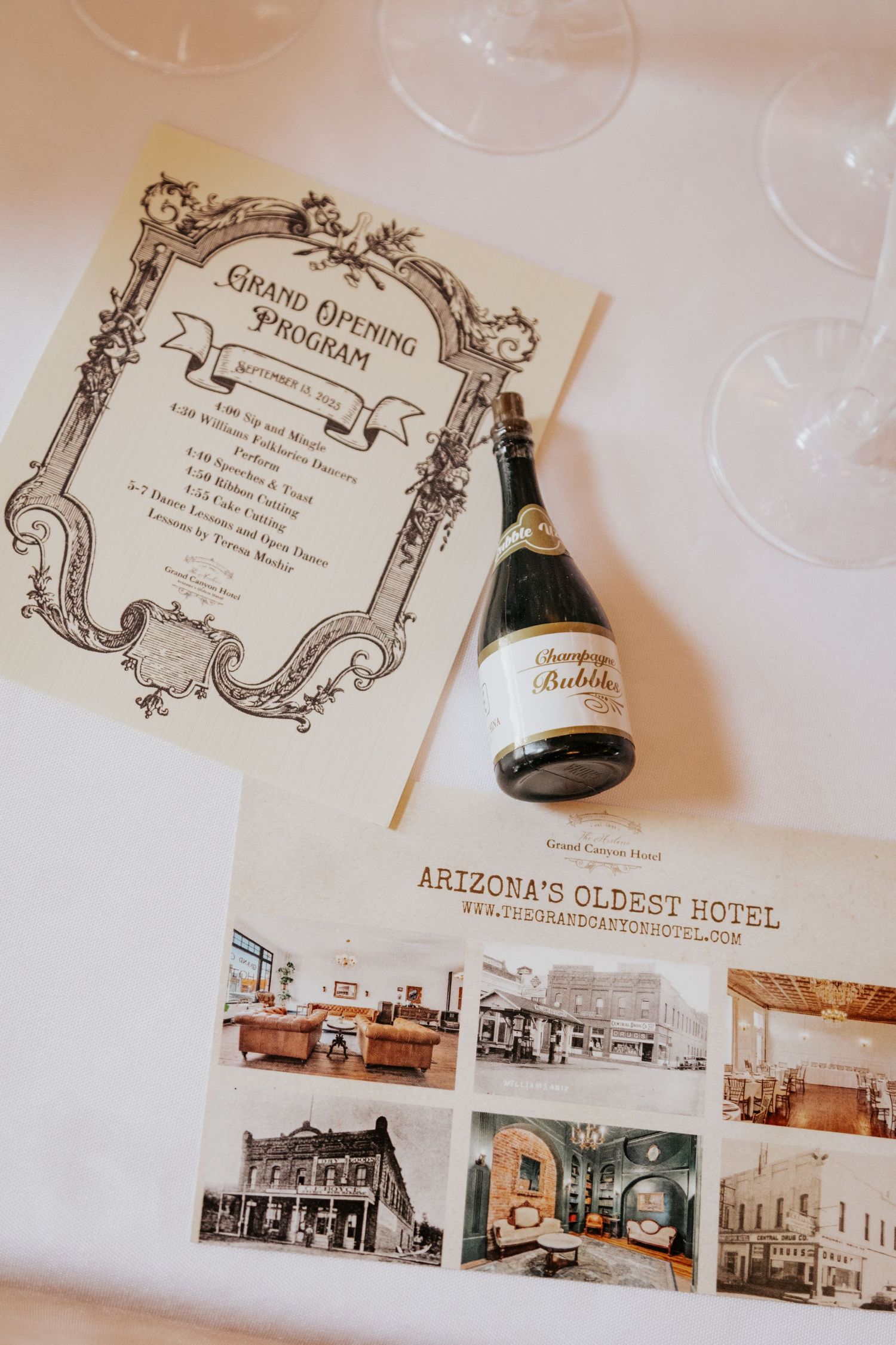 Grand opening program, champagne bottle, and Arizona's Oldest Hotel brochure displayed on a white table.