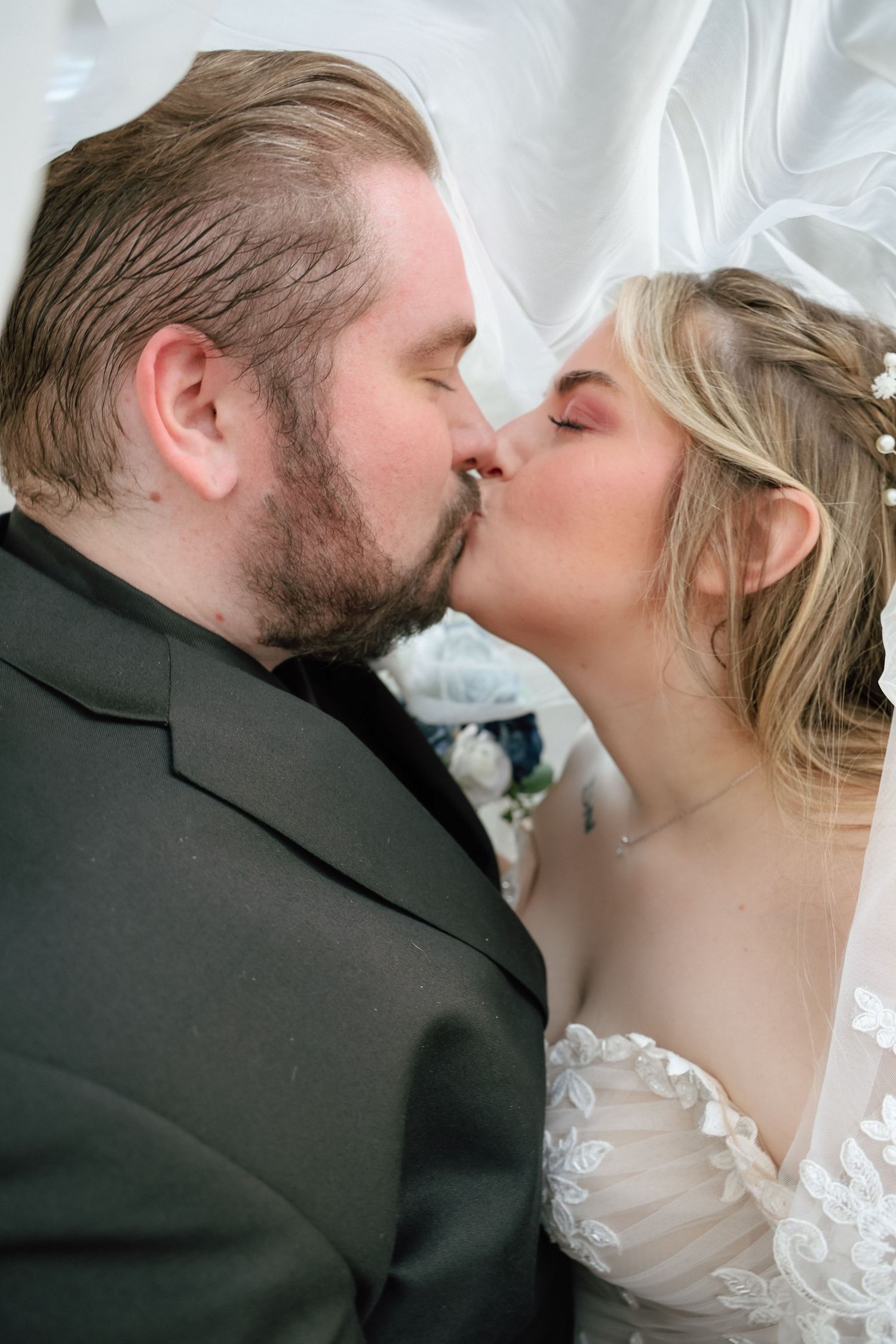 A bride and groom share a romantic kiss under a flowing white veil on their wedding day.