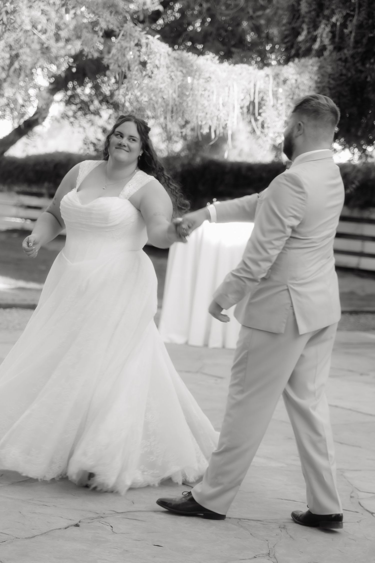 Bride and groom share their first dance outdoors in elegant black and white wedding photo.