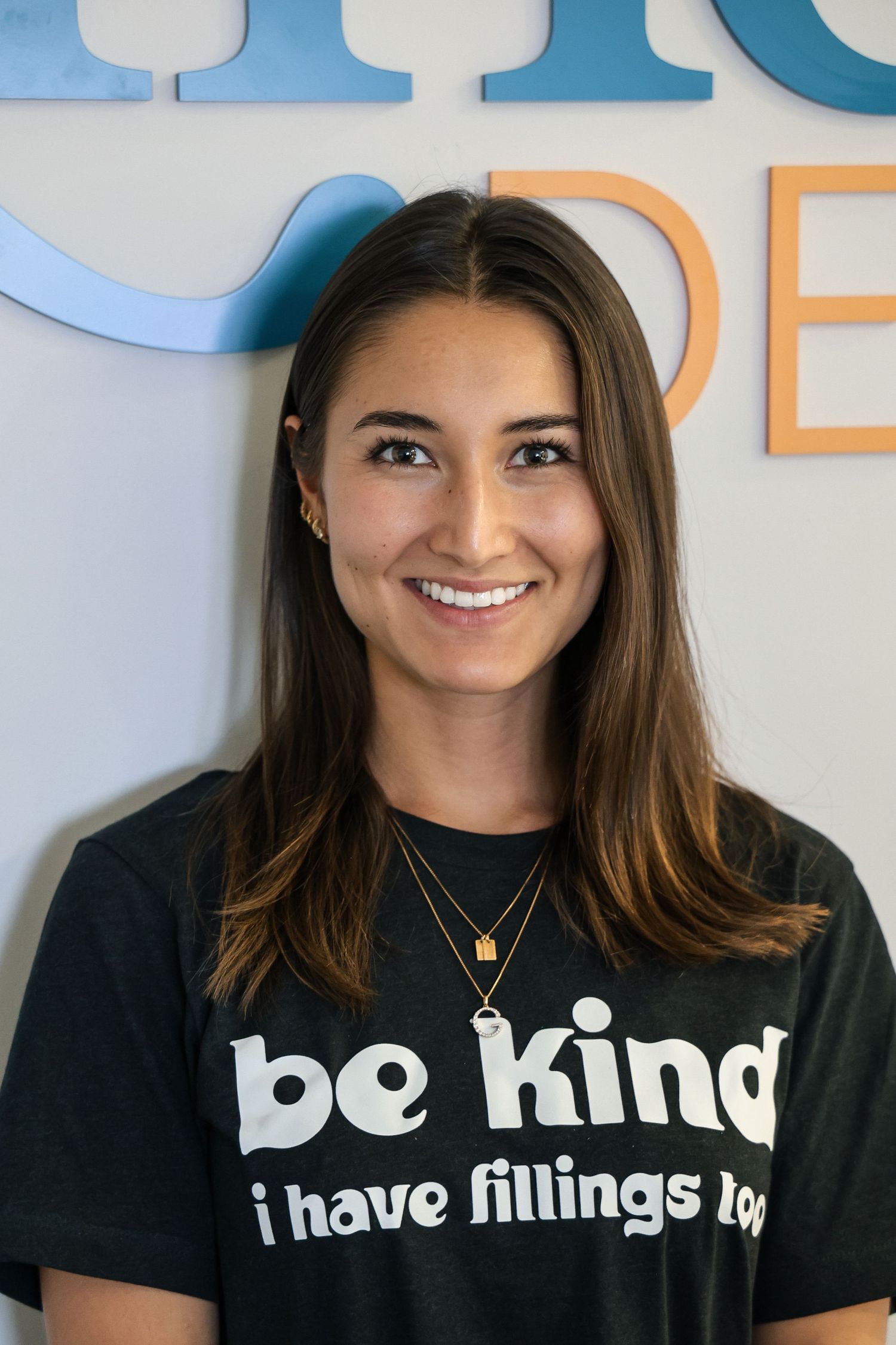 Smiling woman in black 'be kind i have fillings too' dental t-shirt poses in a bright modern dental office.