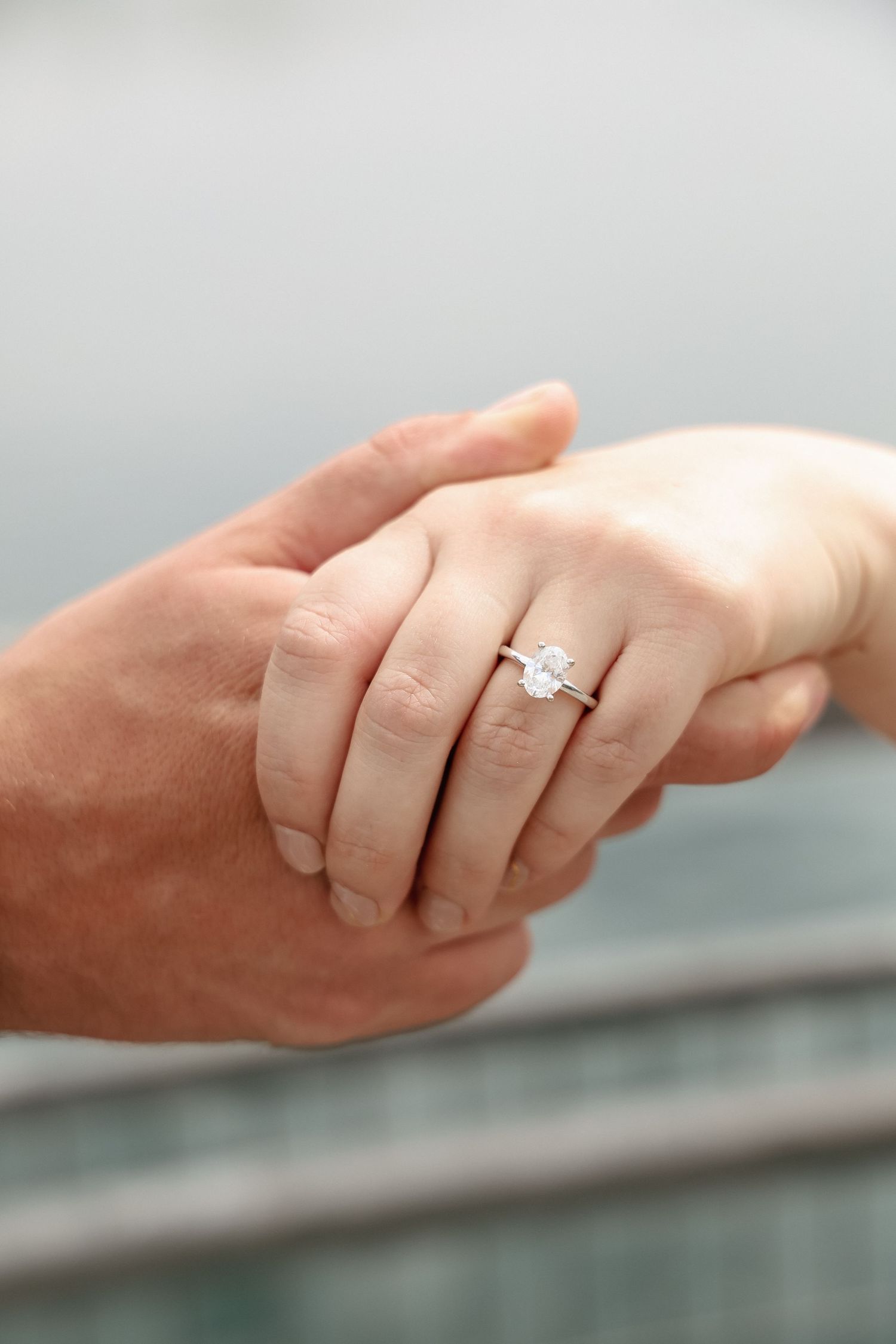 Close-up of two hands holding, woman wearing a elegant solitaire diamond engagement ring on her finger.
