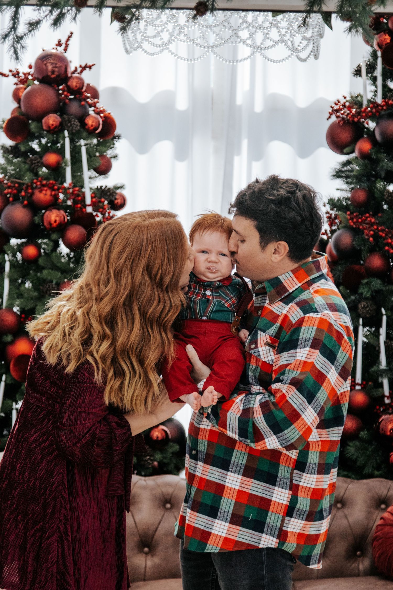 Family shares joyful holiday moments in front of decorated Christmas tree with red ornaments.