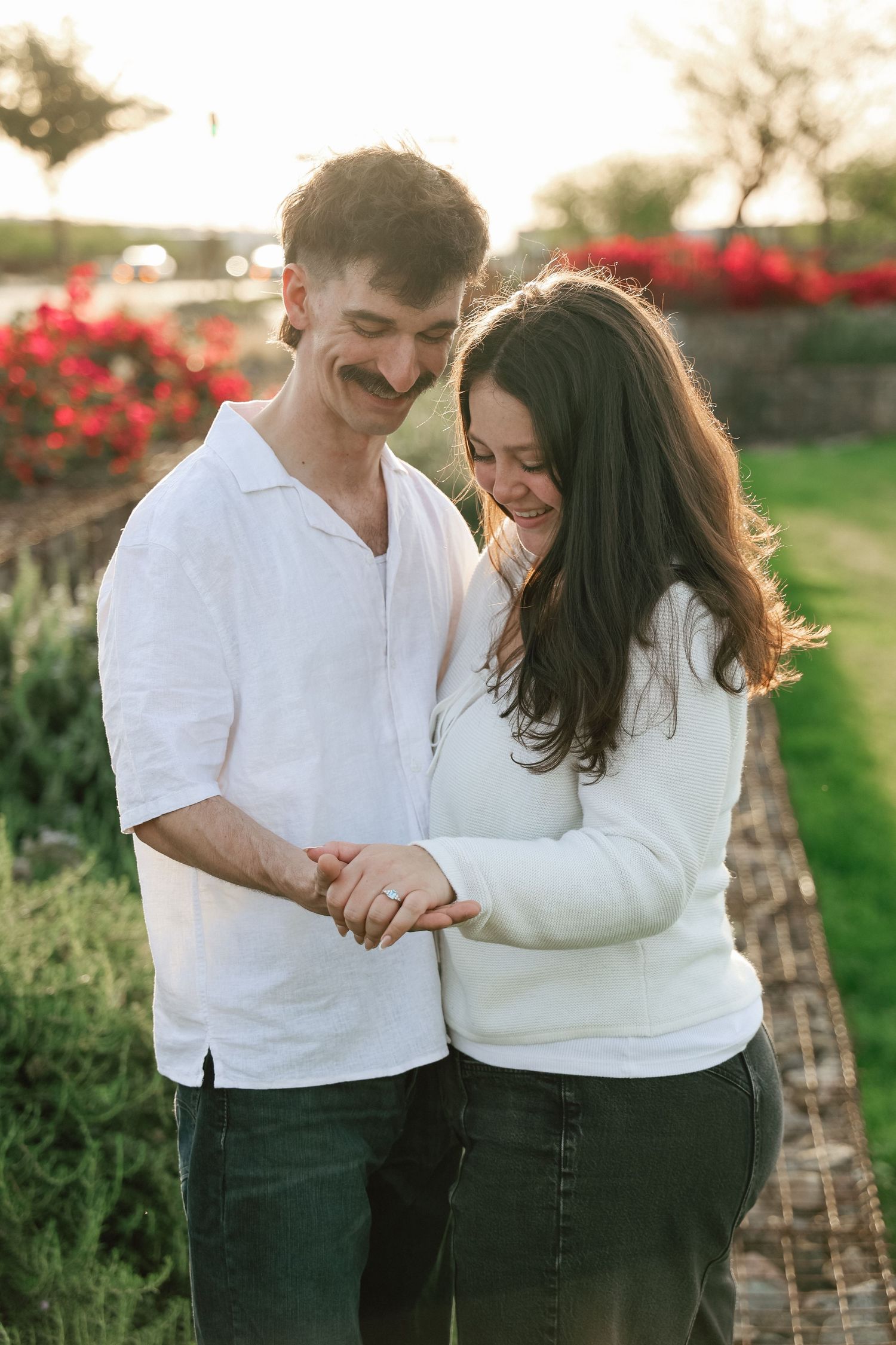 A romantic couple in matching white tops shares tender moments in a garden with red flowers.
