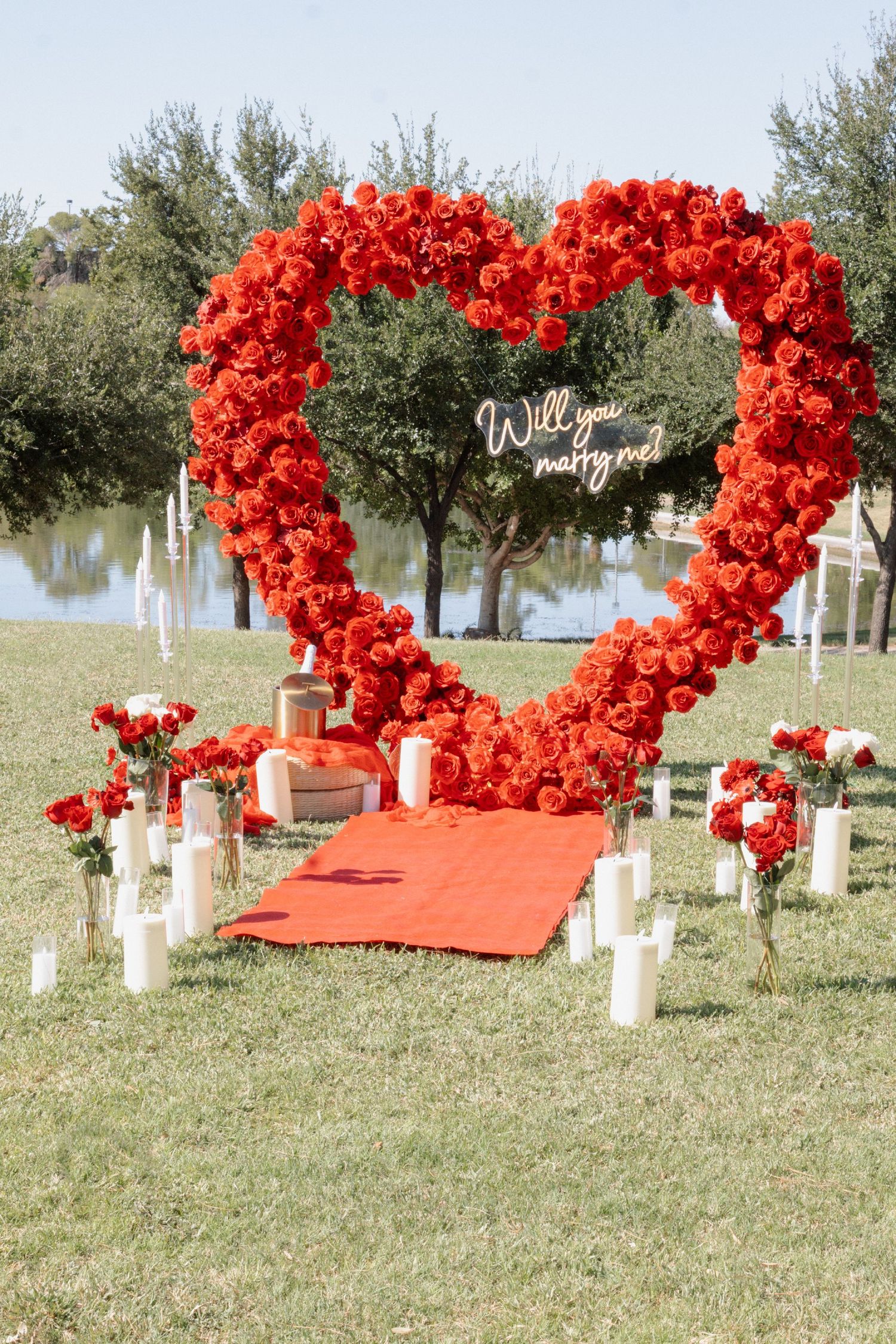 A romantic proposal setup with red balloon heart arches and white decorations on a grassy outdoor area.