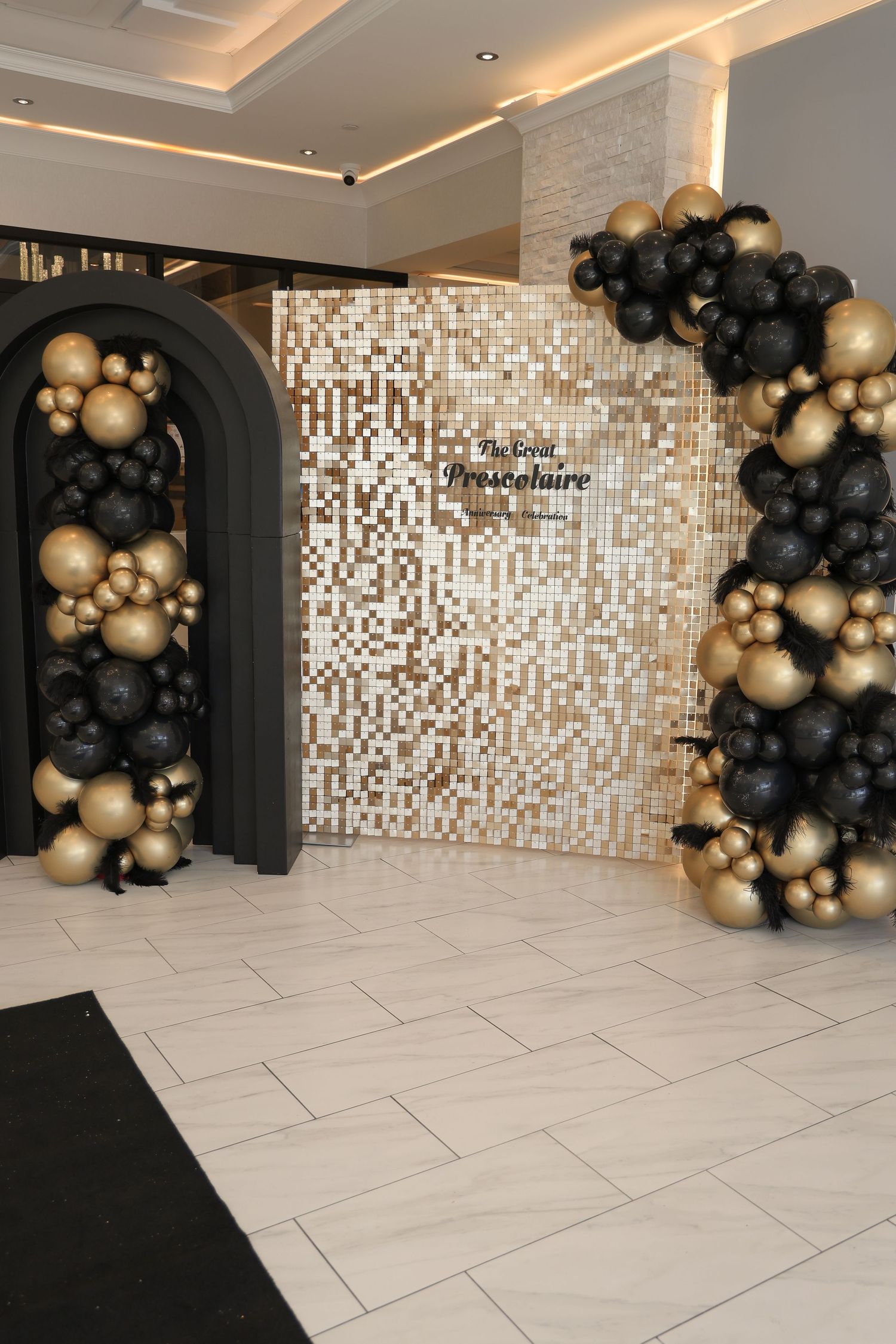 Modern event space with white tile flooring, mosaic tile walls, and elegant black and gold balloon decorations.