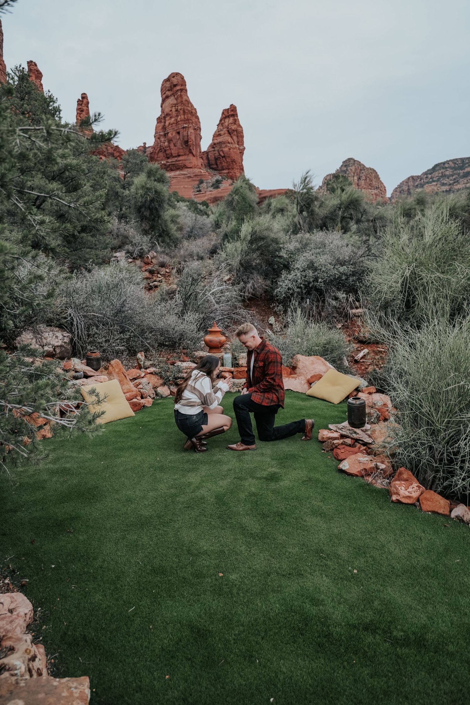 Man proposing to woman on green grass with stunning red rock formations of Sedona, Arizona in the background.