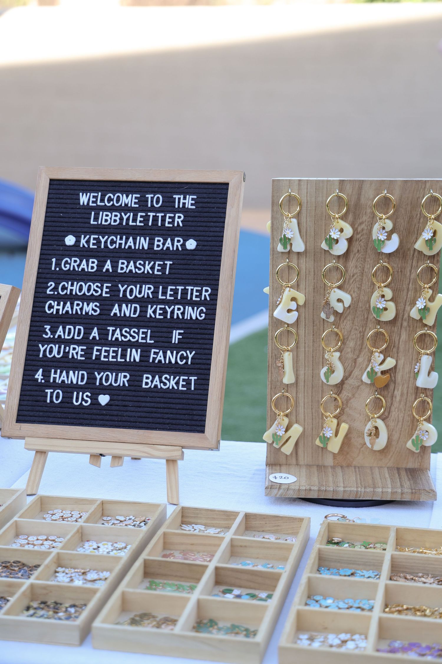 Display of letter charms and keyrings with instructional signs for customization at a retail kiosk.
