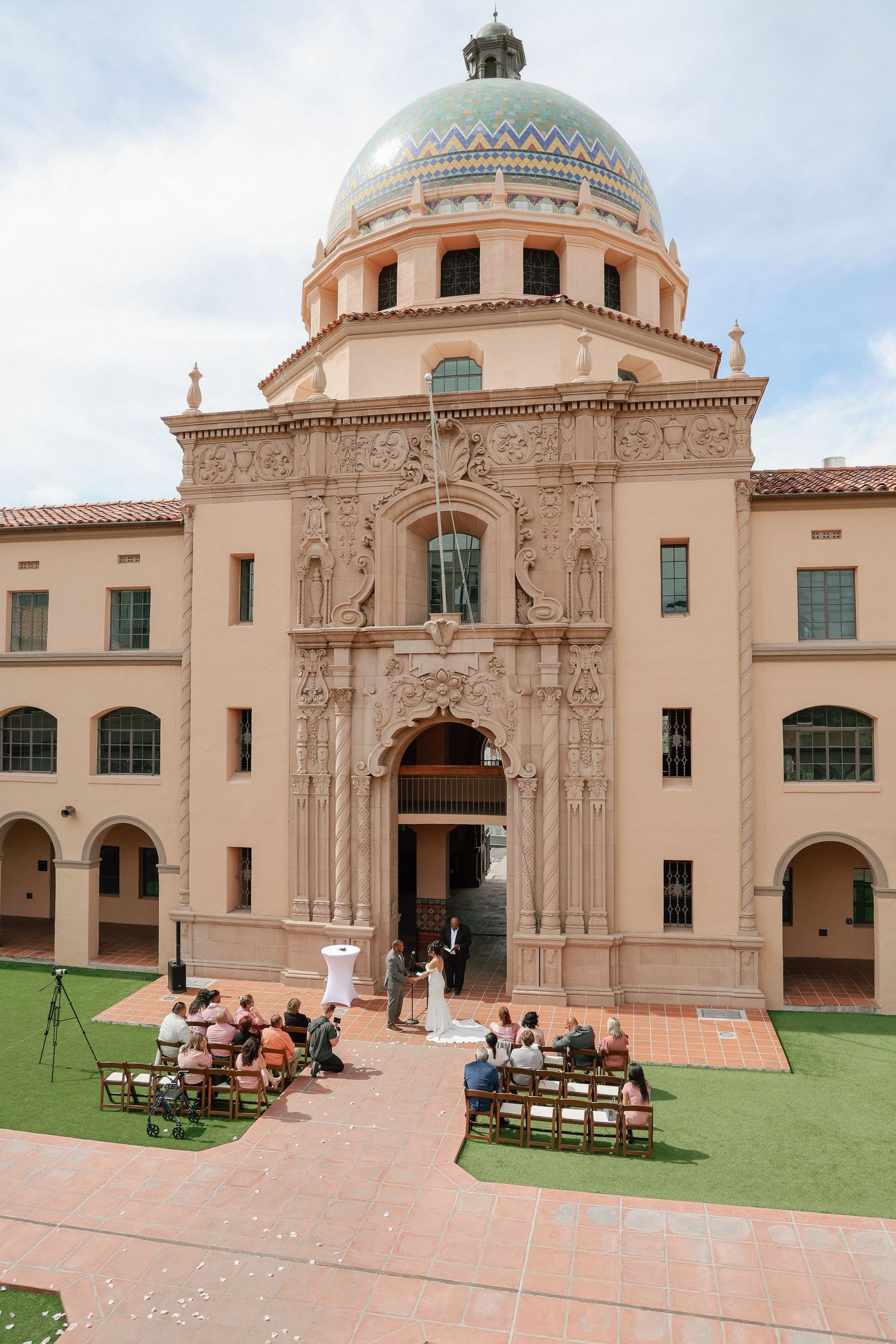 Outdoor wedding ceremony in front of an ornate Spanish Colonial Revival building with a green dome.