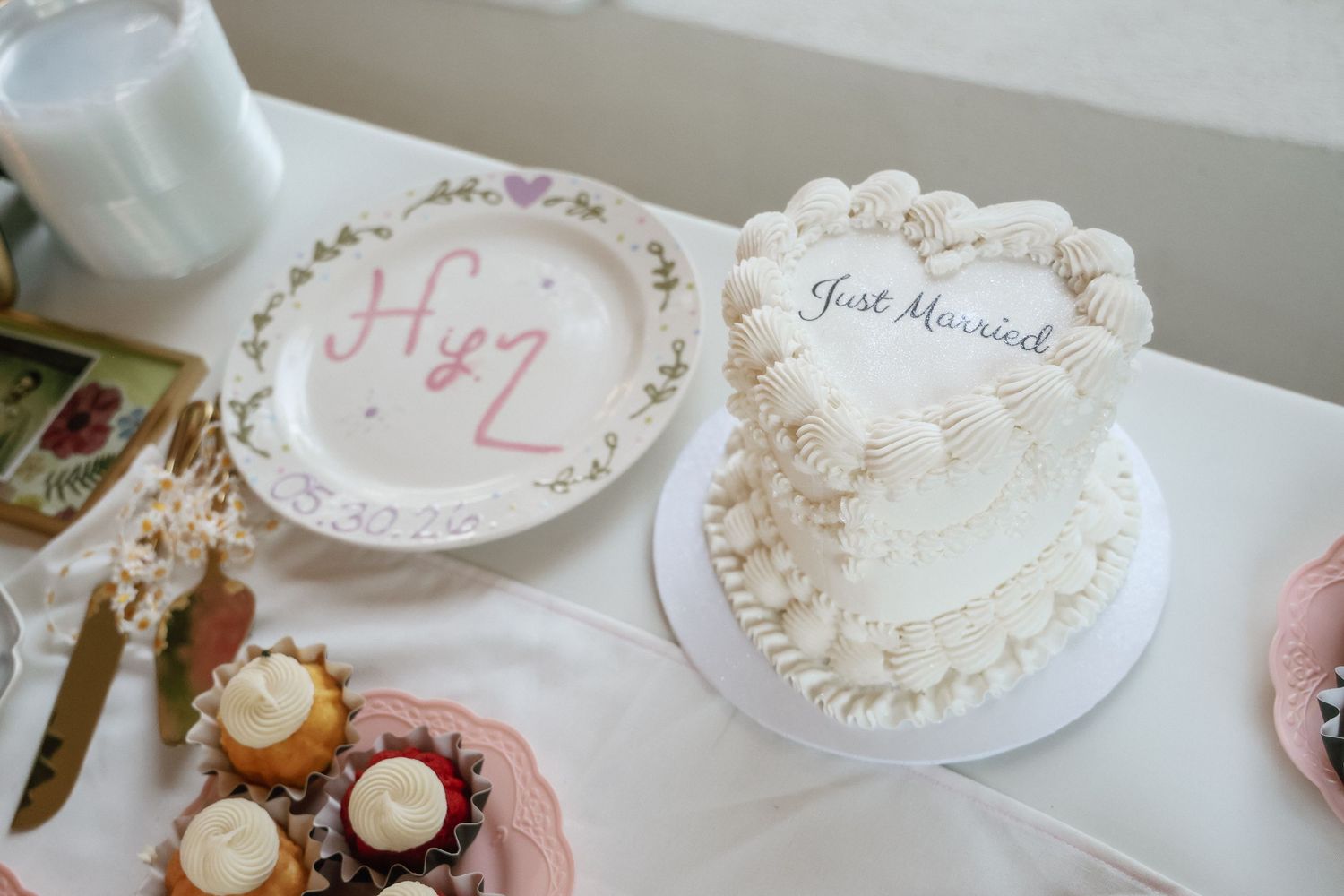 A white heart-shaped Just Married wedding cake beside a decorative plate with H+Z on a white table.