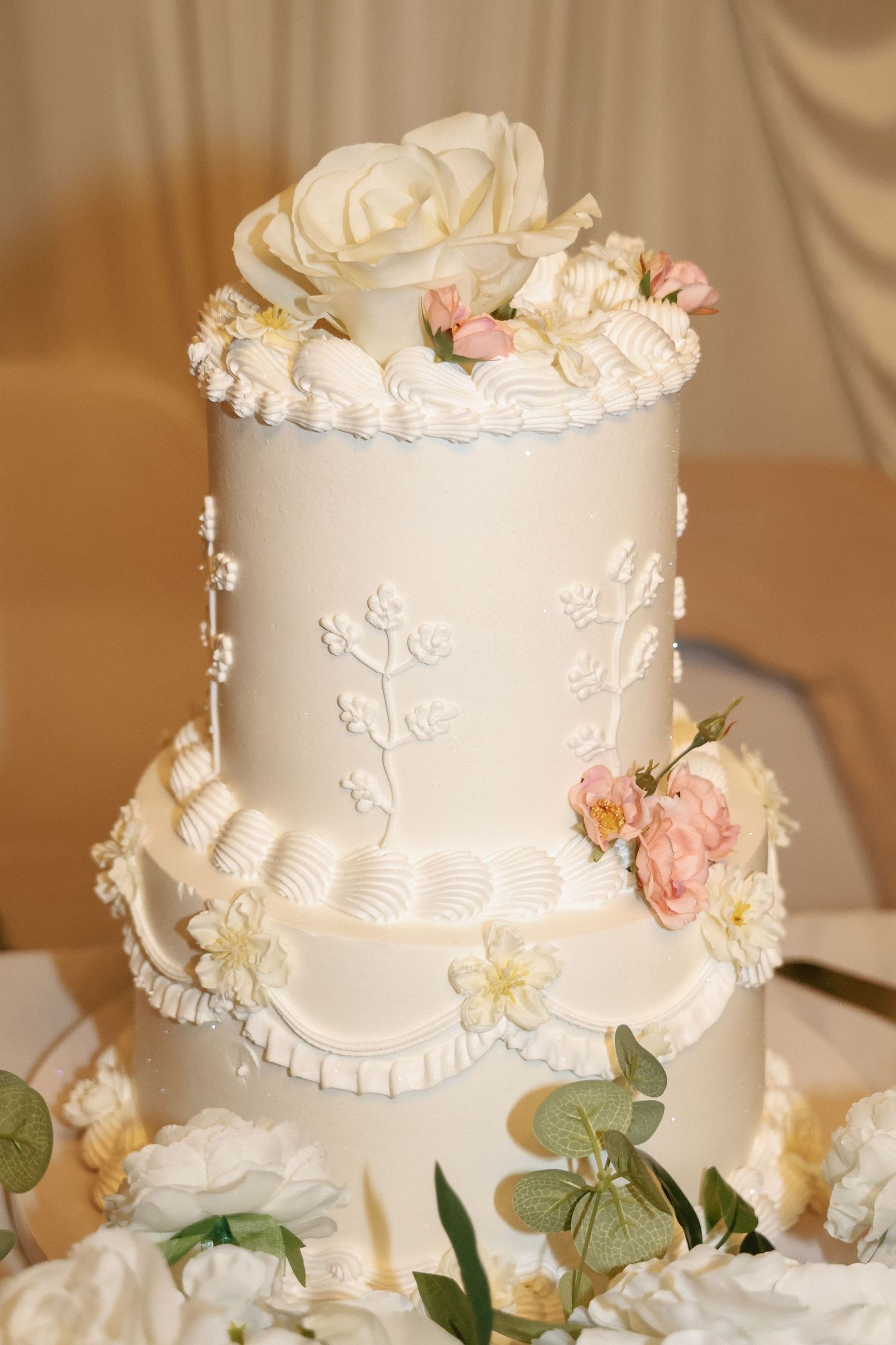 Elegant two-tier white wedding cake with floral decorations, pink roses, and intricate fondant detailing on display.