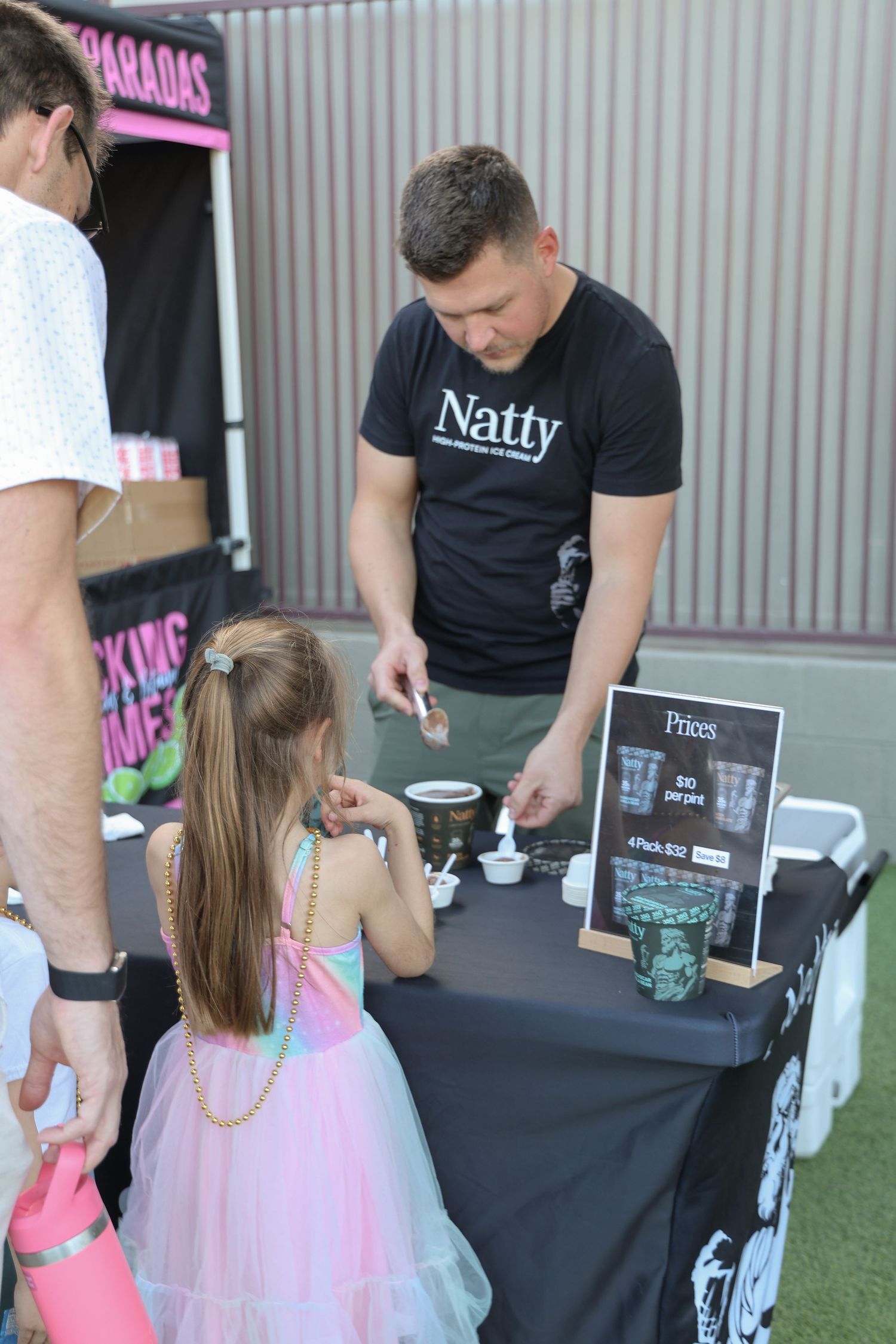 Children in tutus visiting activity stations at an outdoor event with black-draped tables.