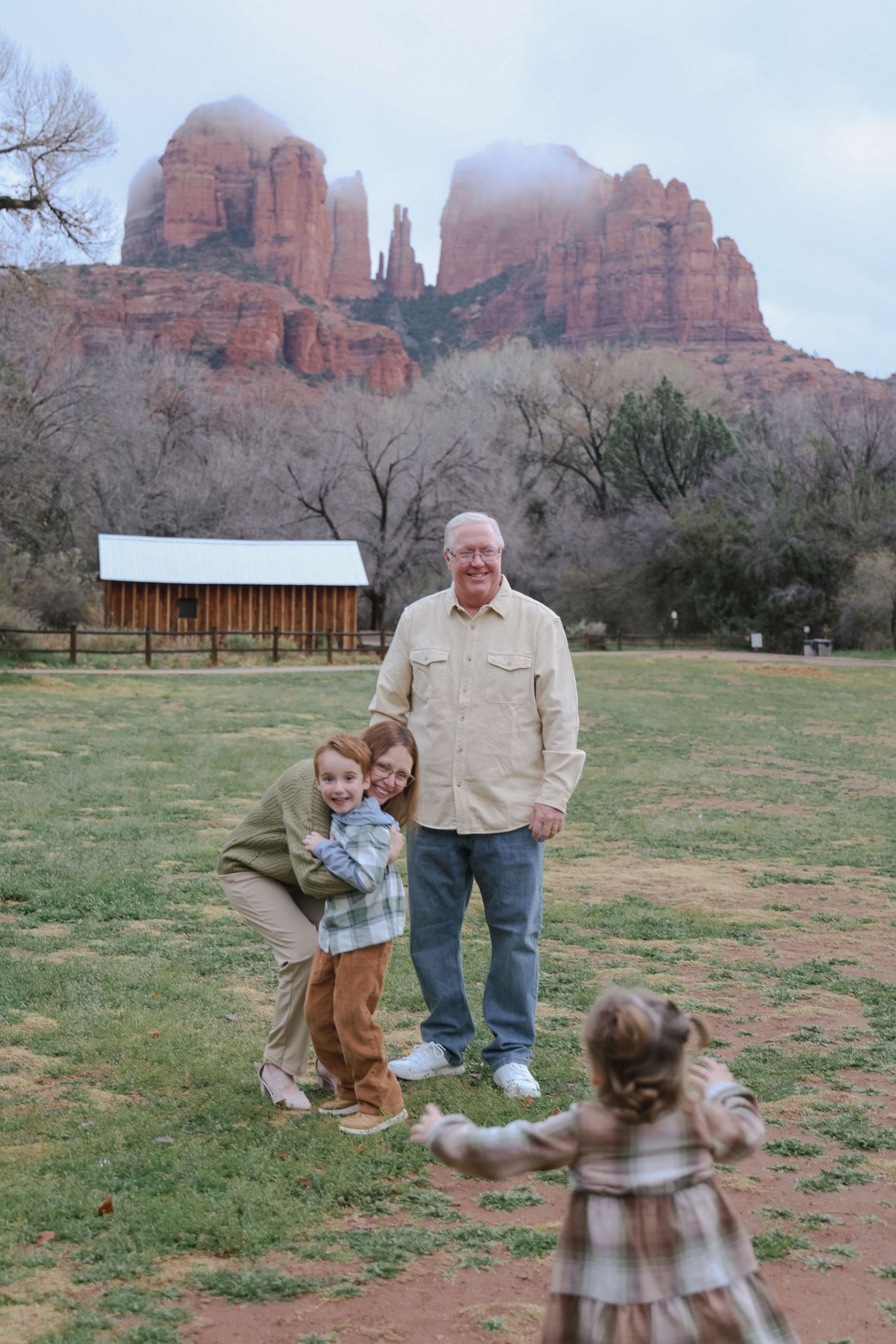 Family gathering at Cathedral Rock in Sedona with rustic cabin and red rock formations in background.