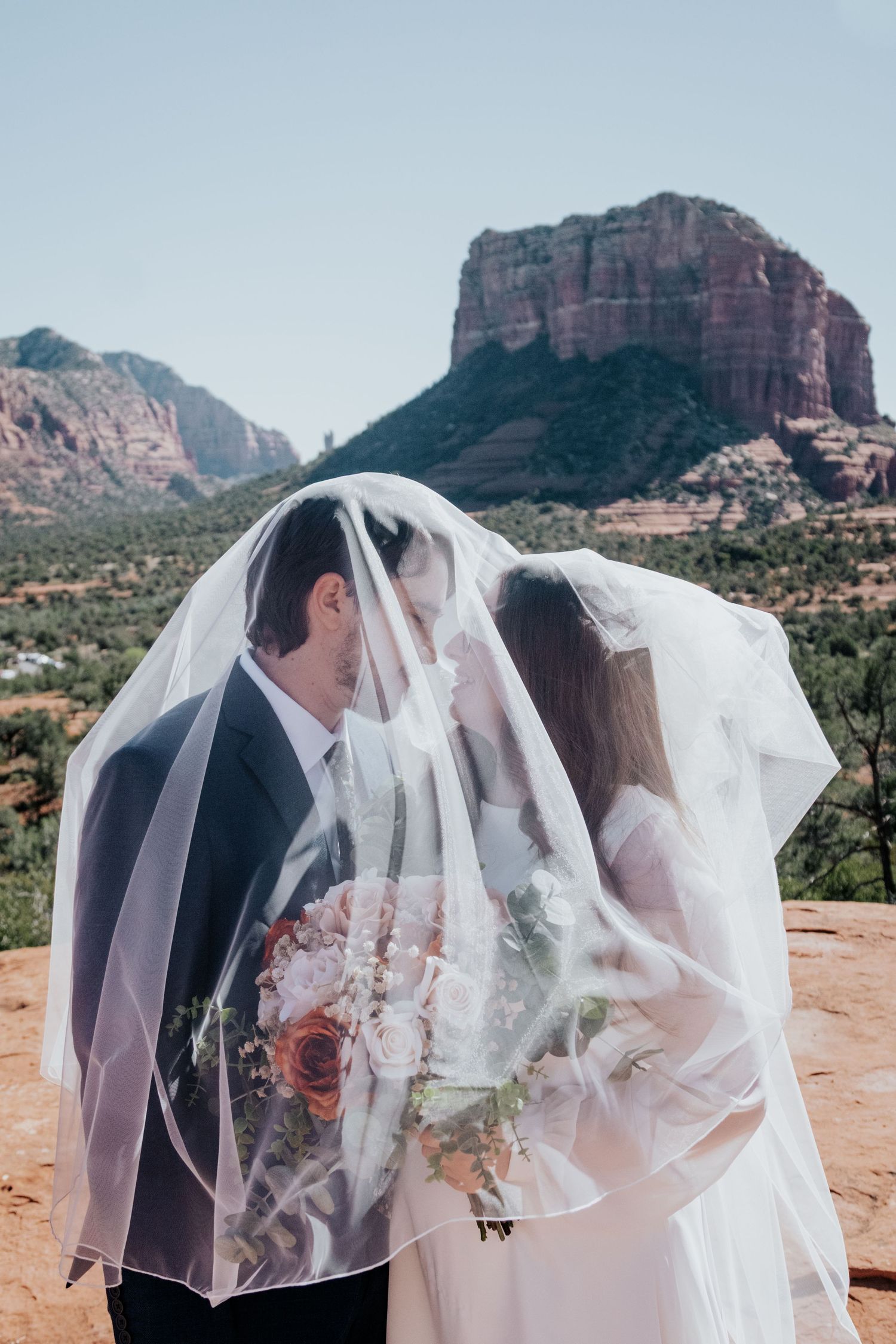Wedding couple sharing intimate moments under a flowing veil with desert mountains in background.
