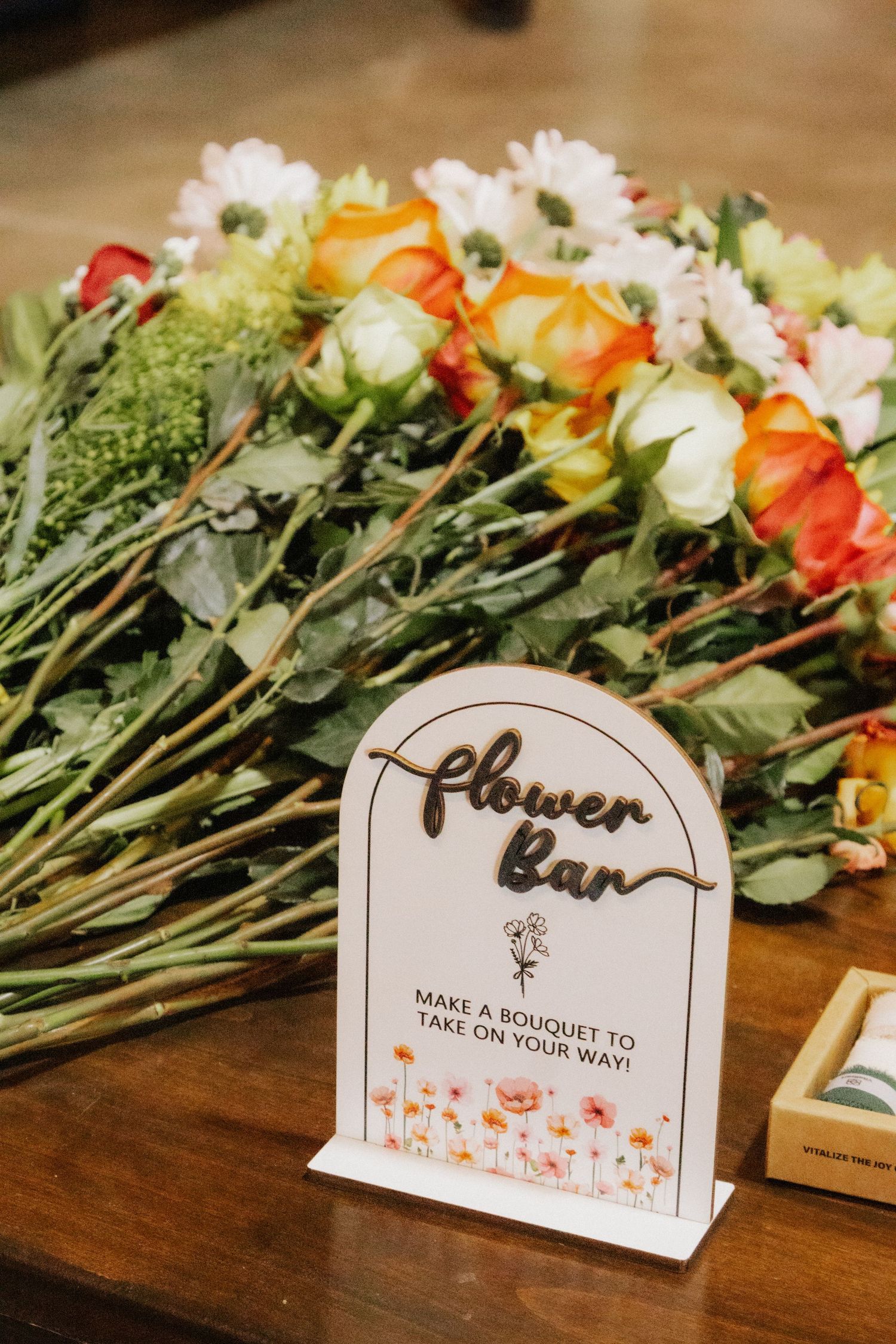 Wooden flower bar sign with fresh floral arrangements displayed on rustic table.