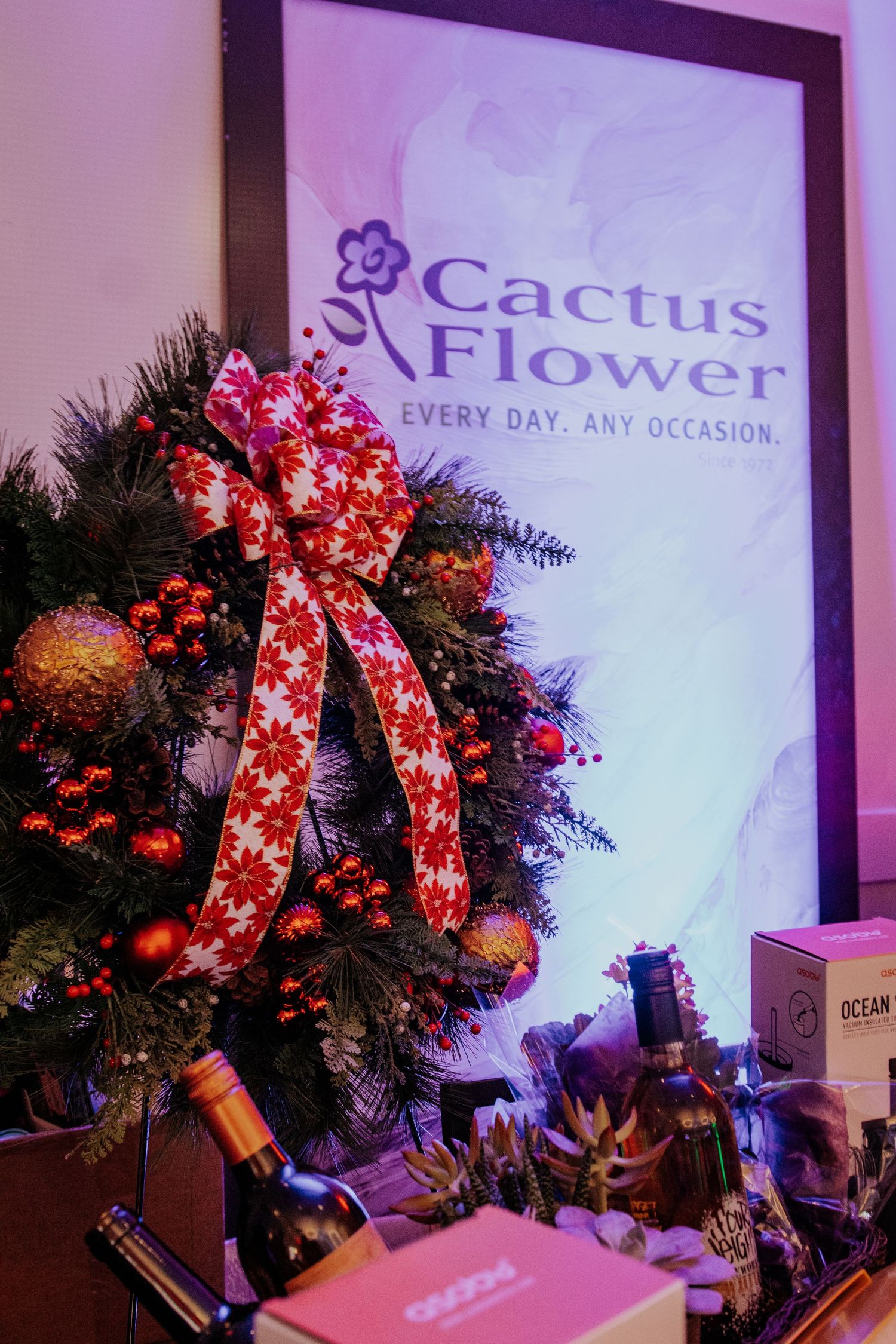 Holiday wreaths with red bows and ornaments displayed against a Cactus & Flower branded wall.