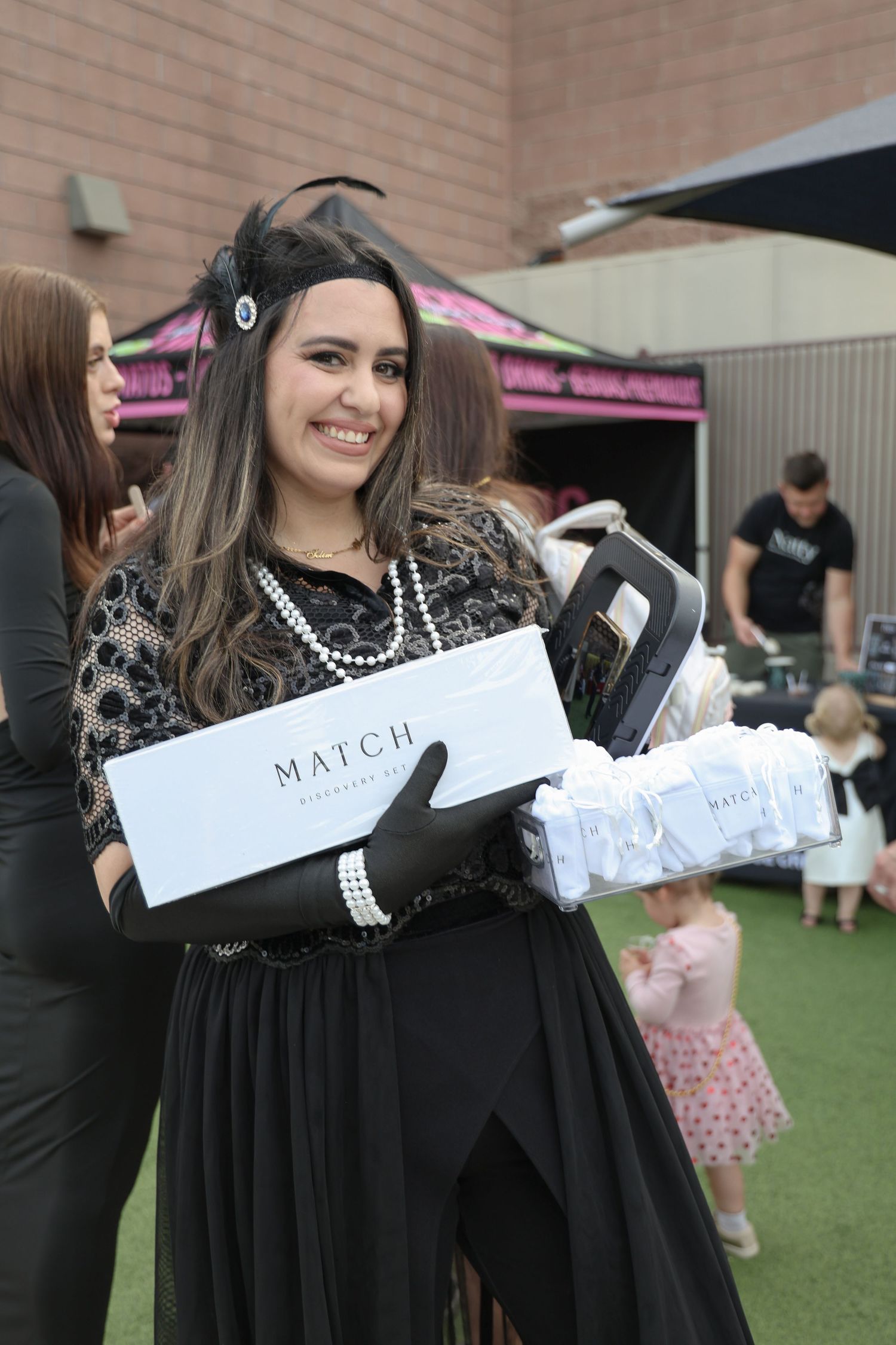 A group of graduates in black gowns gather outdoors holding white envelopes during a graduation ceremony.