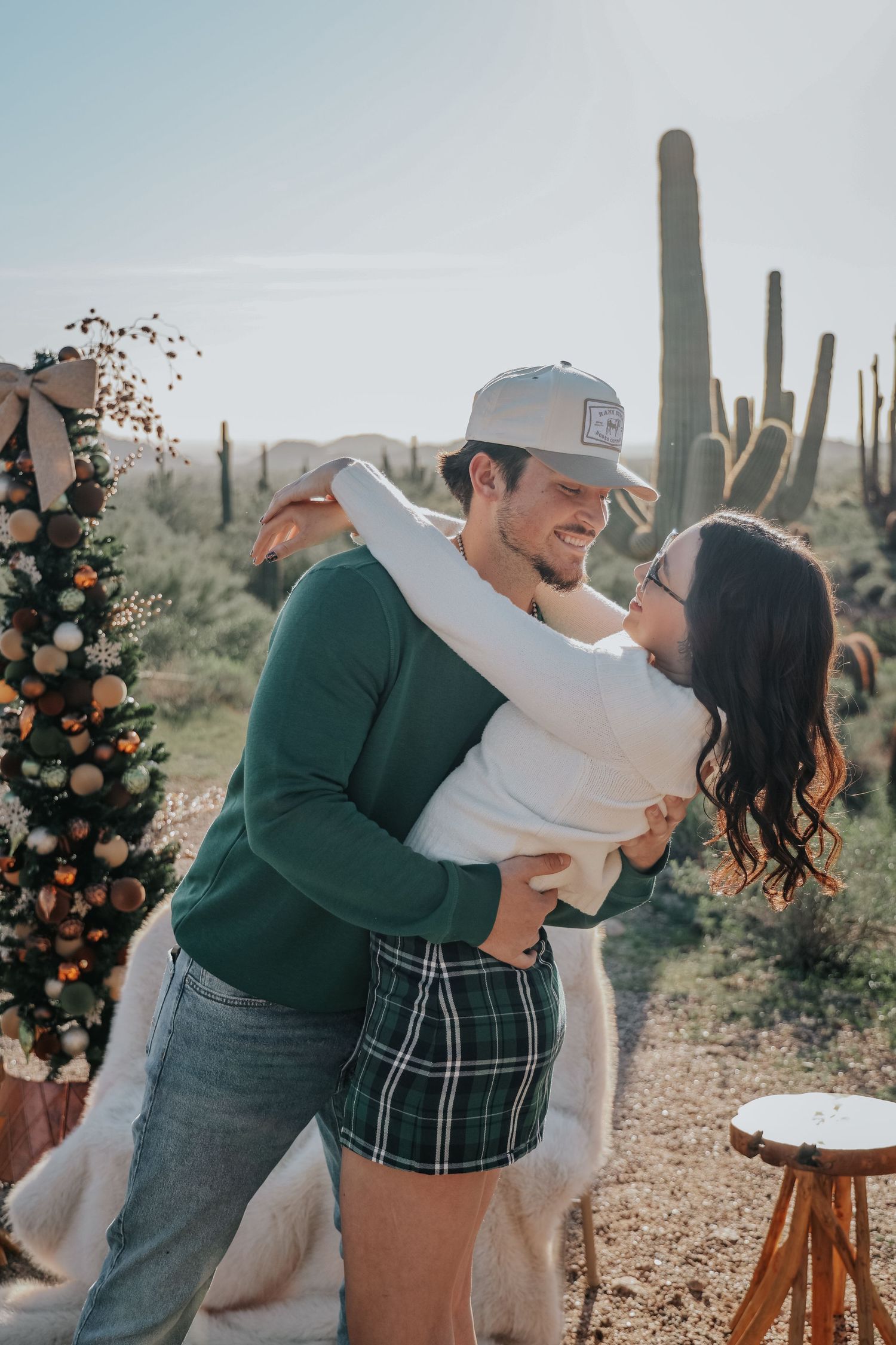Couple dancing and embracing near a decorated Christmas tree in a desert landscape with tall saguaro cacti in Arizona.