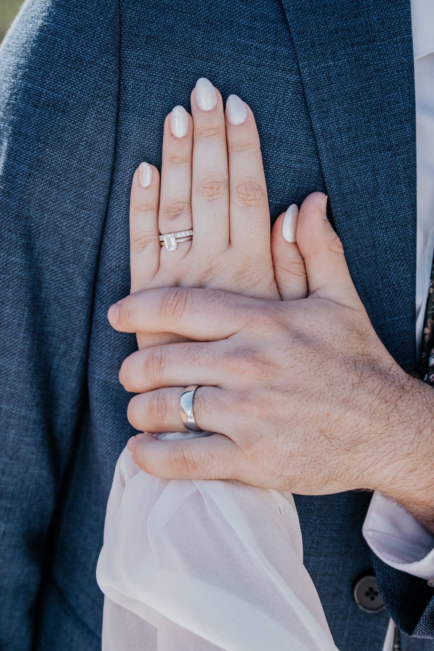 Close-up detail shots of wedding rings and hands against a navy blue suit jacket.