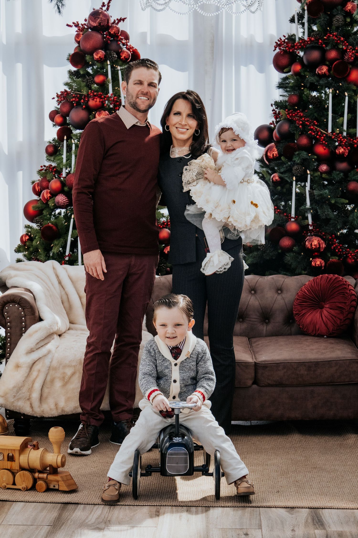 Family Christmas portraits with decorated tree and brown leather couch in bright studio.