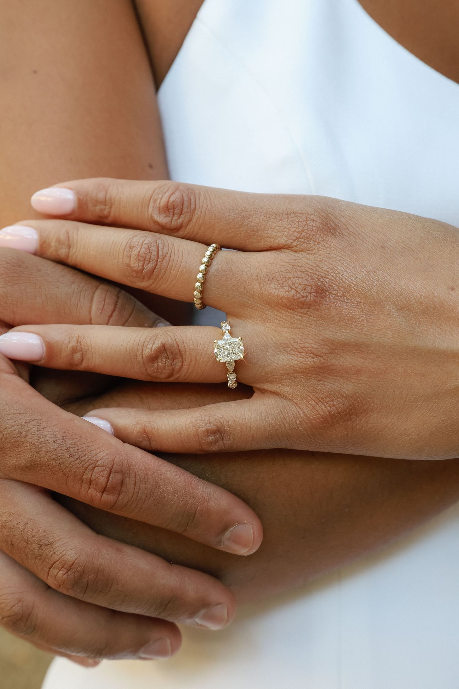 Close-up of a woman's hand wearing a diamond solitaire engagement ring and gold beaded band on her ring finger.