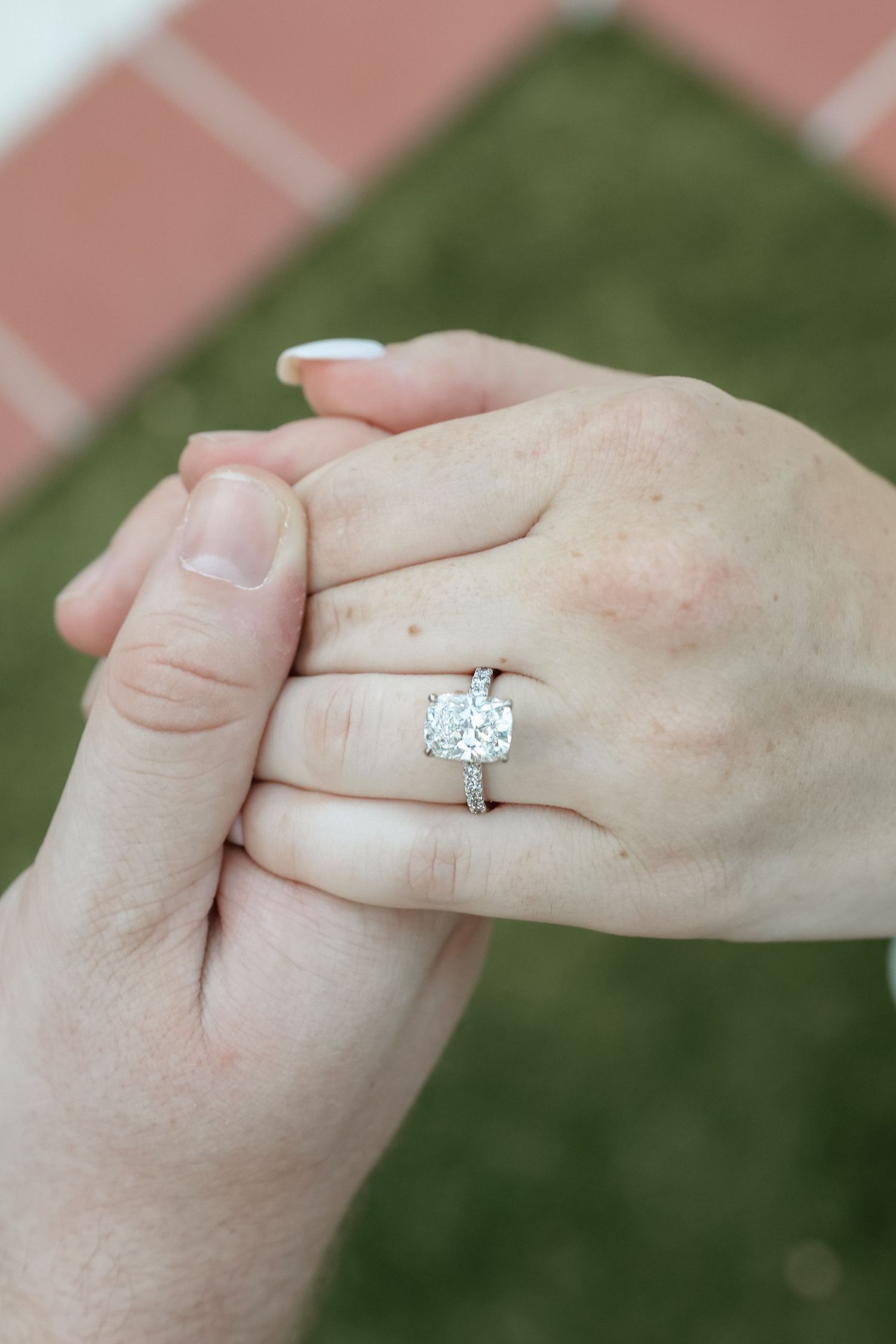 Close-up of hands holding, showcasing a stunning cushion-cut diamond engagement ring on a silver band.