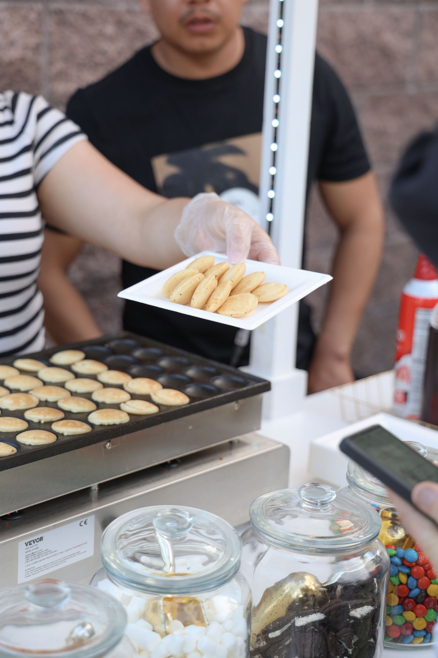 Food sampling station with glass jars and serving trays set up on a white table.