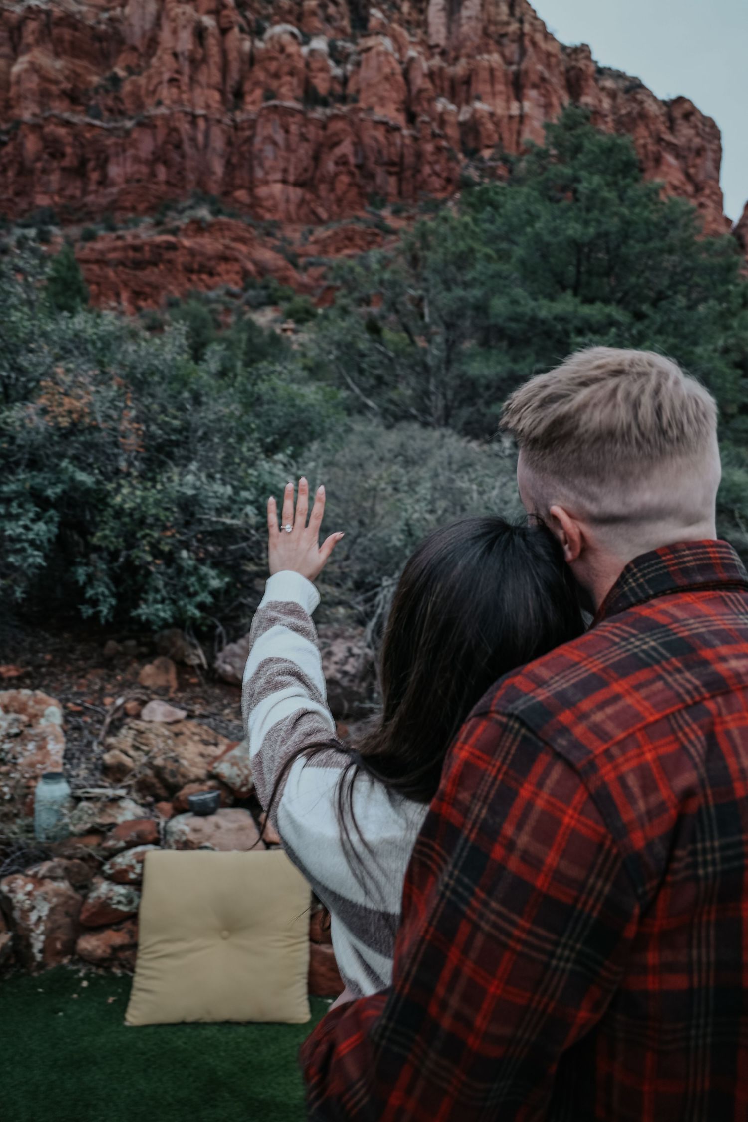 Couple in casual attire embracing near red rock formations at sunset.