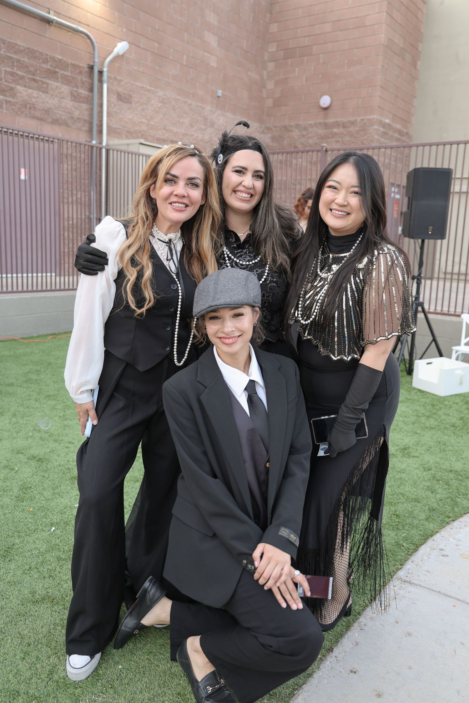 A group wearing black formal attire posing together outdoors near a brick building.