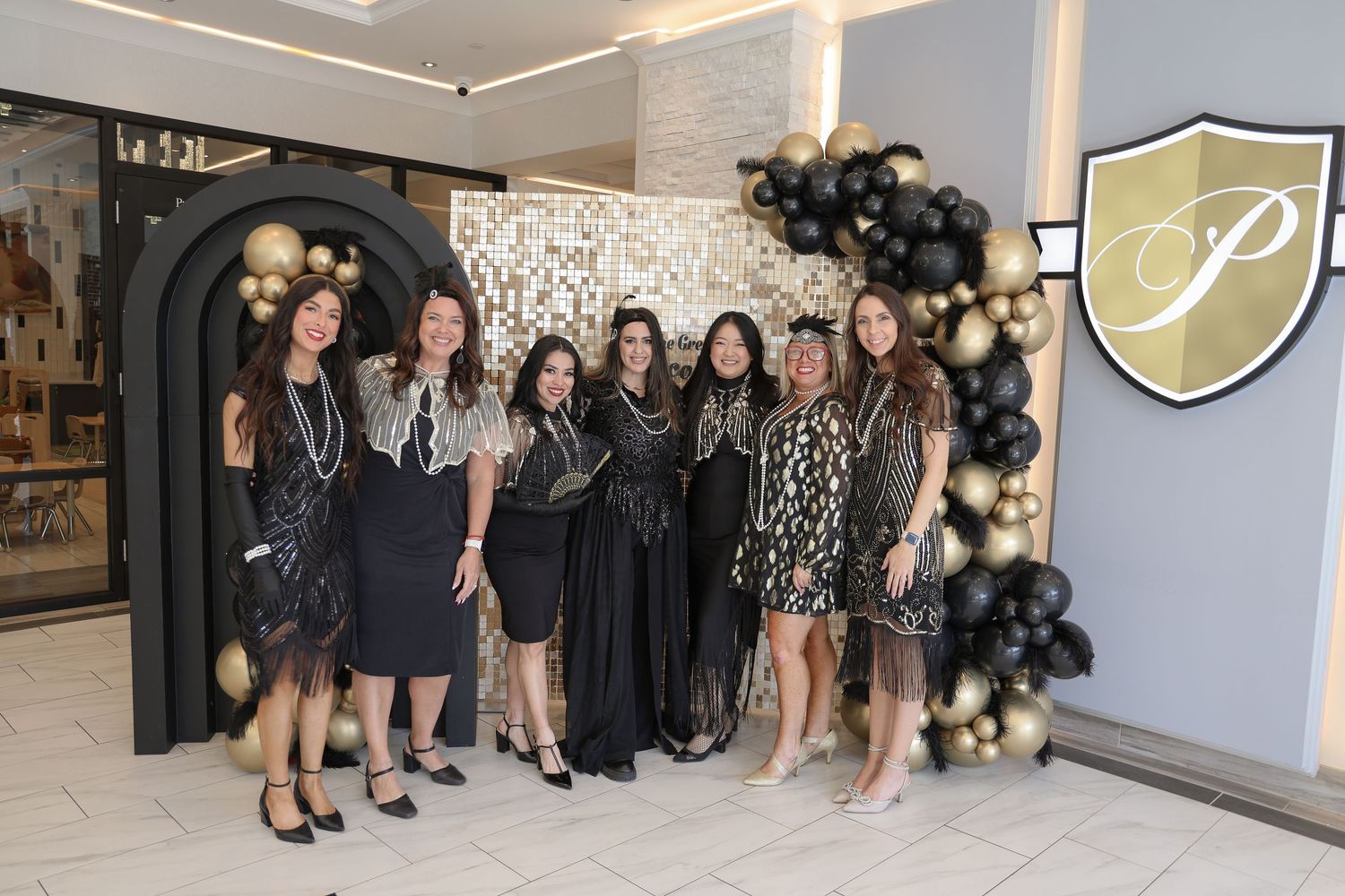 A group poses together at a formal event wearing black dresses and attire against a light colored wall.