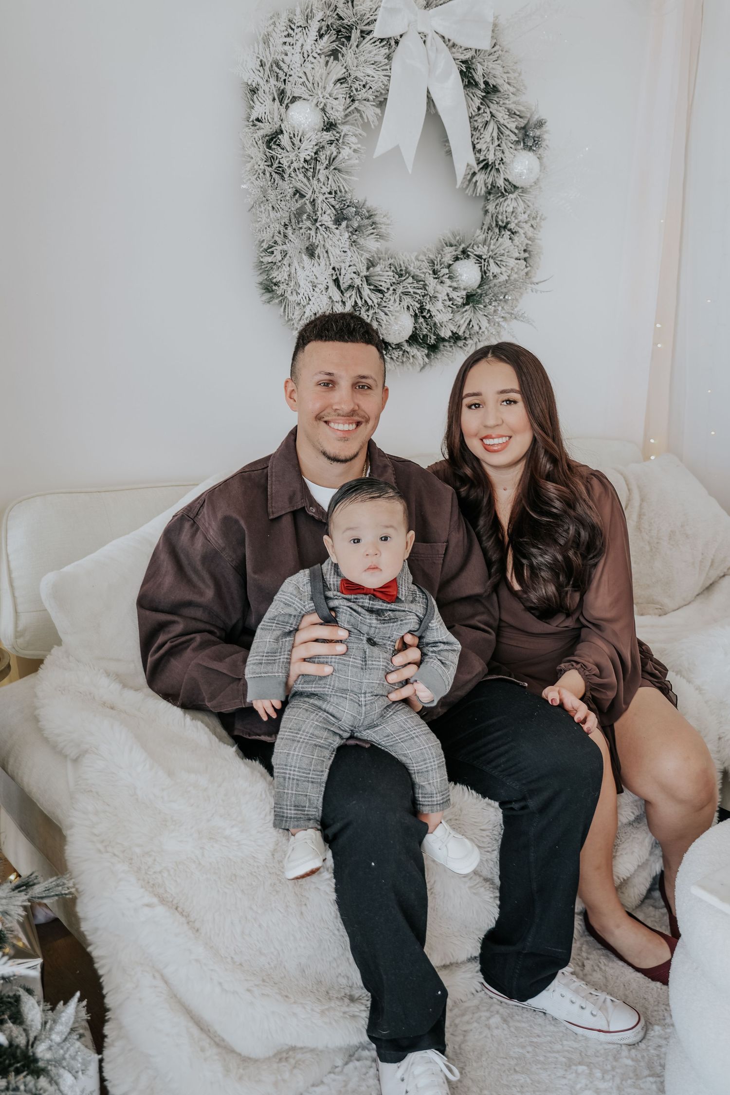Family sits together on white couch with holiday wreath decor in background.