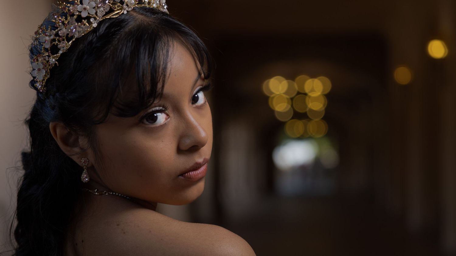 Quinceañera wearing an ornate crown tiara and earrings poses elegantly for a quinceañera portrait photo.