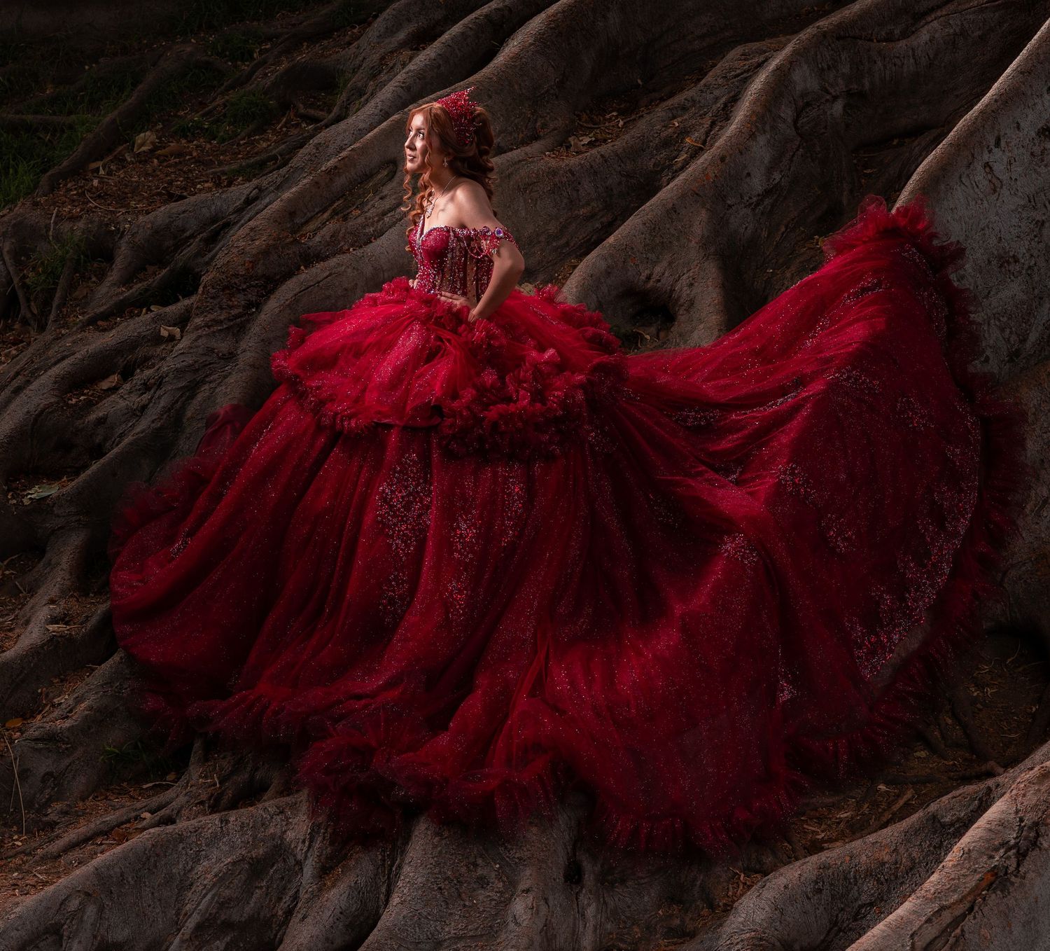 A dramatic red ball gown with flowing tulle skirt photographed against dark rocky terrain at dusk.