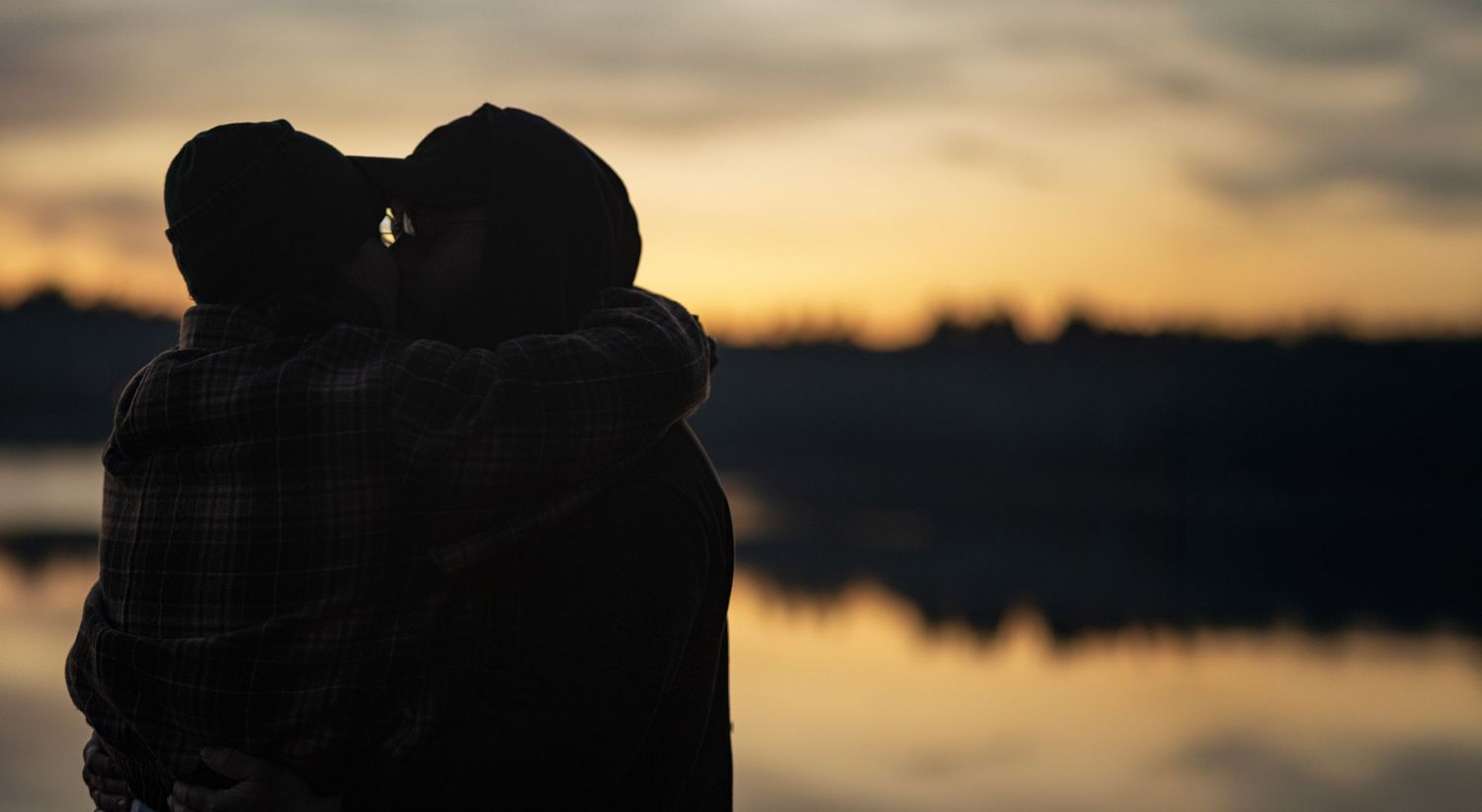 Silhouettes of couple against golden sunset sky over calm water. At an engagement photoshoot