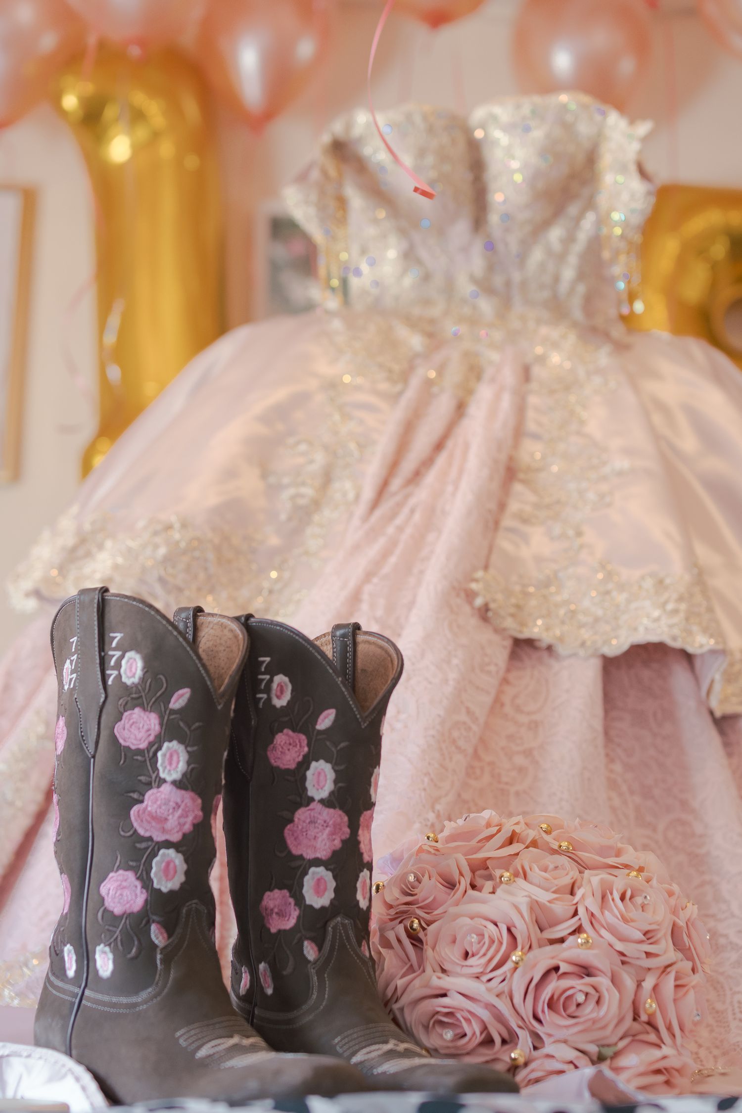 Pink quinceañera dress with floral details and decorative cowboy boots arranged for a photo. At a Quinceañera