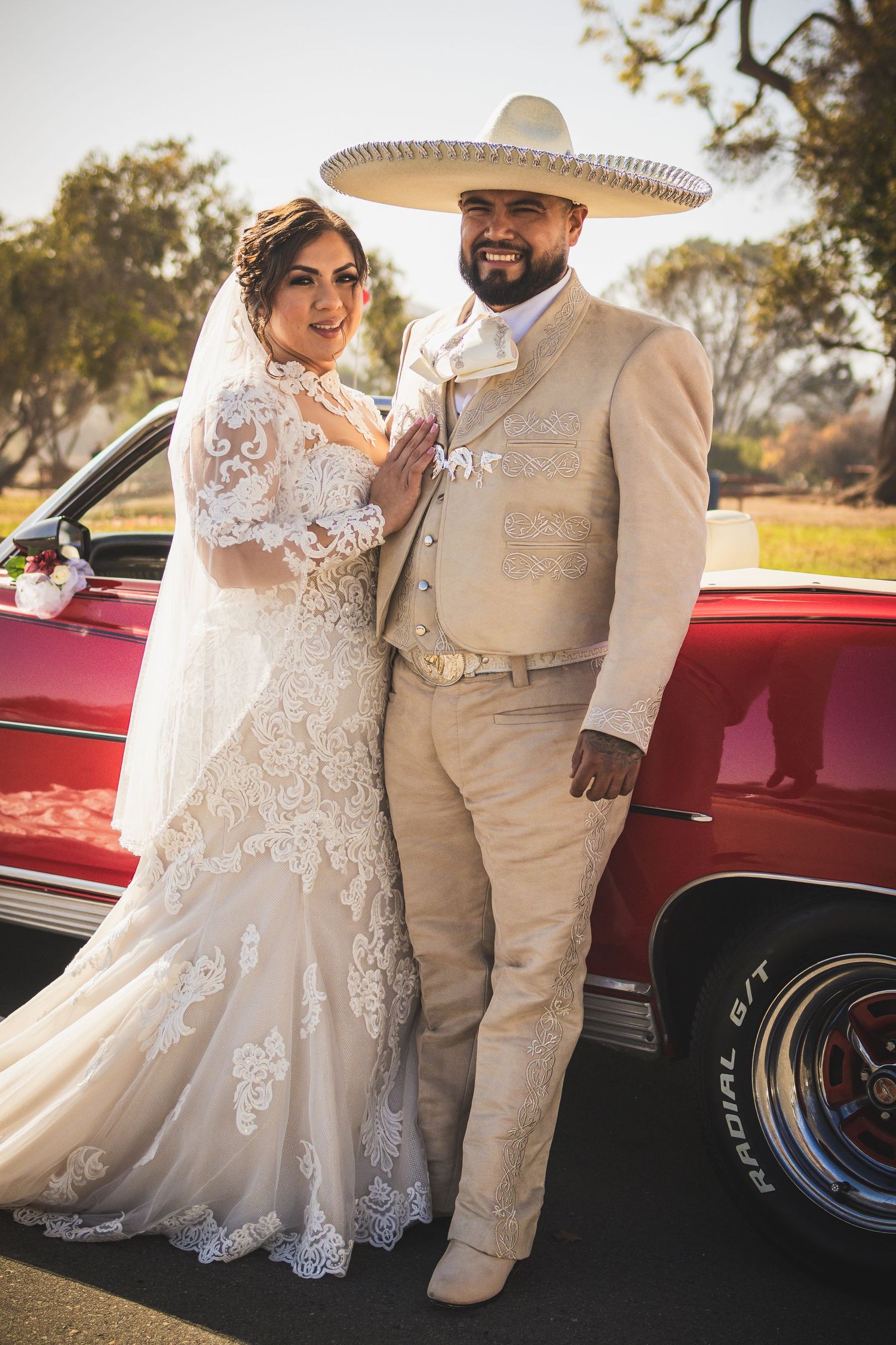 Romantic wedding portraits with couple in white dress and beige suit next to vintage red car. At San Luis Rey Parish celebrating a wedding