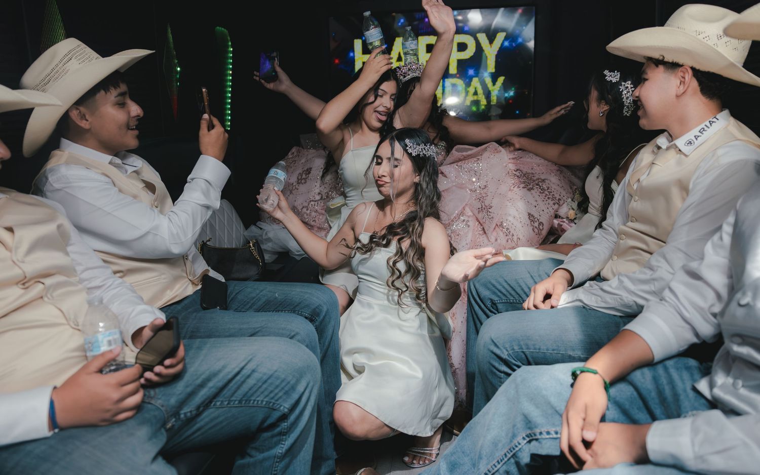 Young woman in white dress celebrates birthday in limo with friends wearing cowboy hats and jeans.