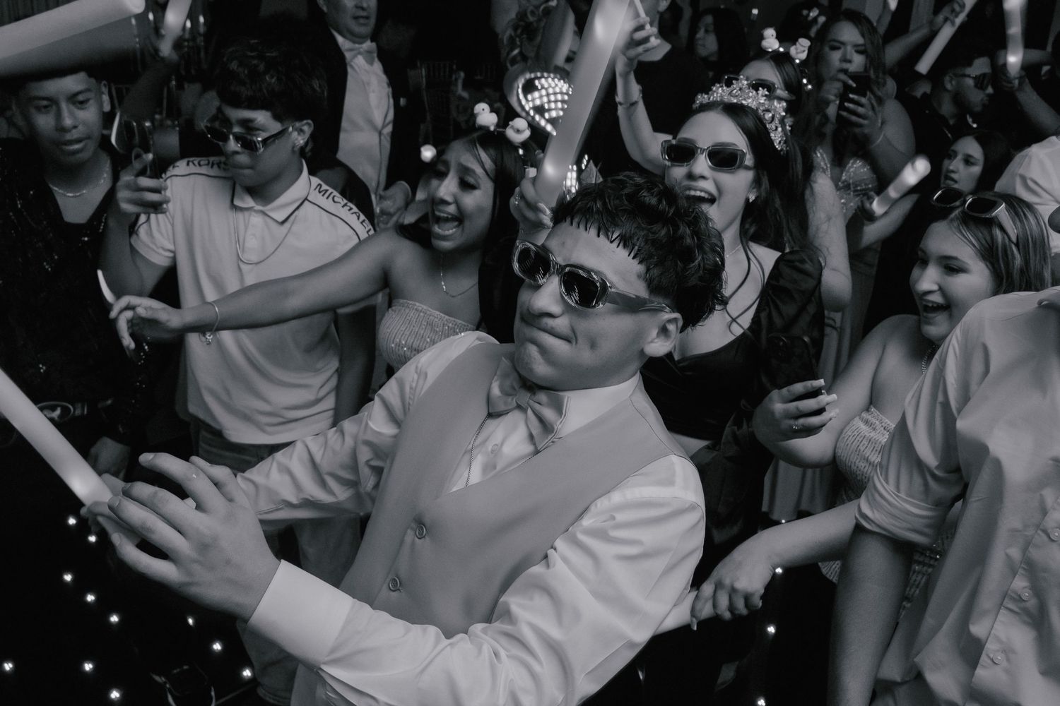 A black and white photo collage shows a lively crowd of people dancing and celebrating at what appears to be a party or event.
