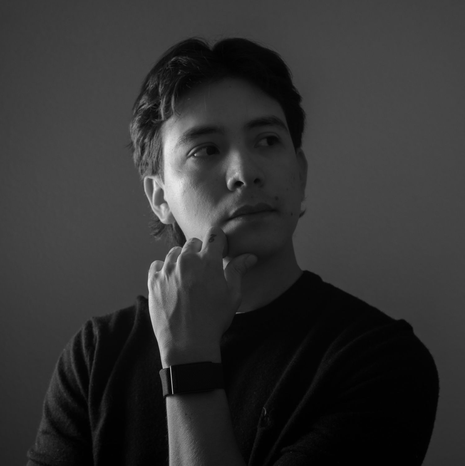 Black and white portrait of a thoughtful young man in a dark sweater with a watch, hand on chin.