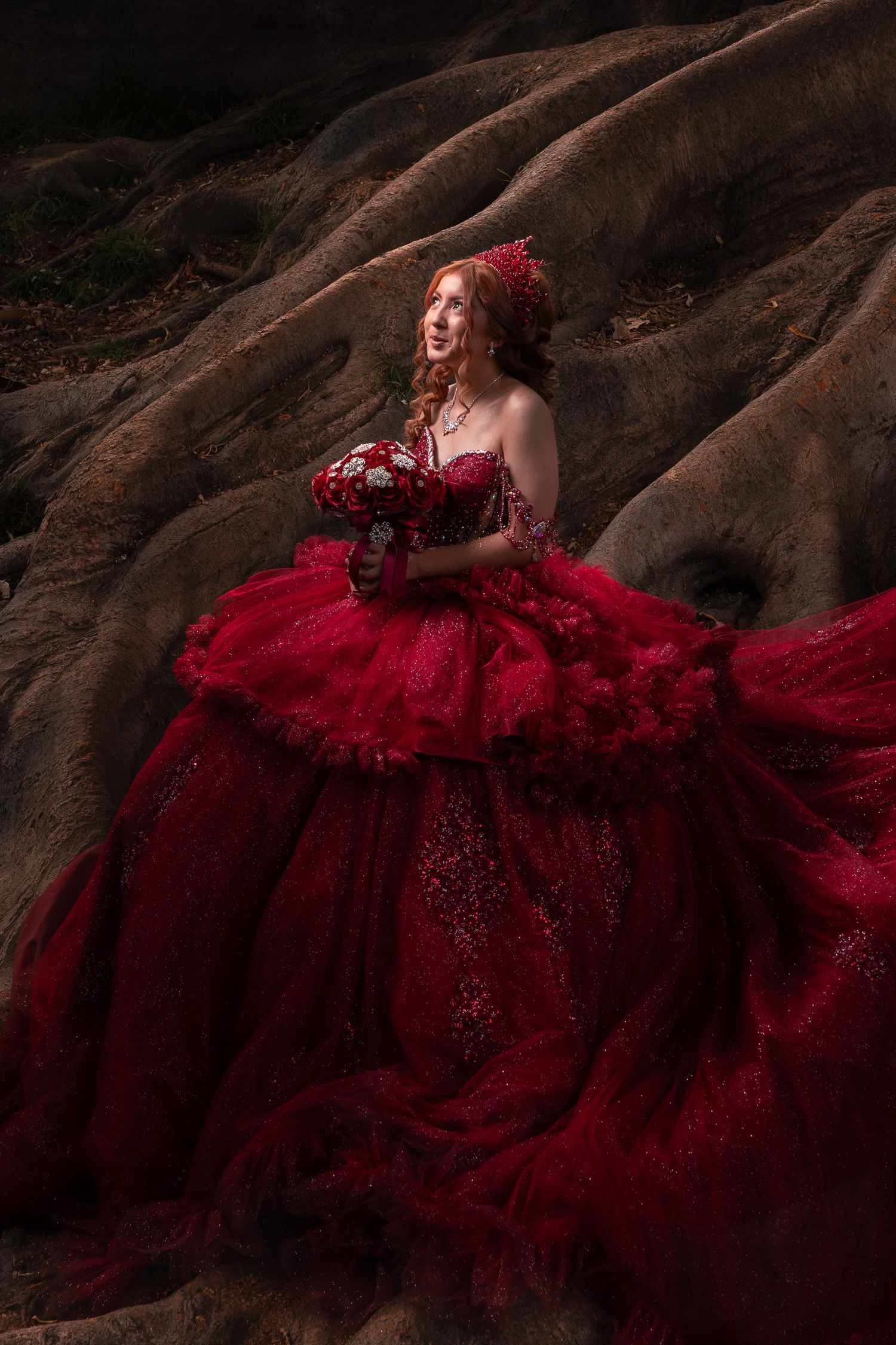 A dramatic fashion portrait featuring a flowing deep red gown against rugged rock formations in moody lighting.
