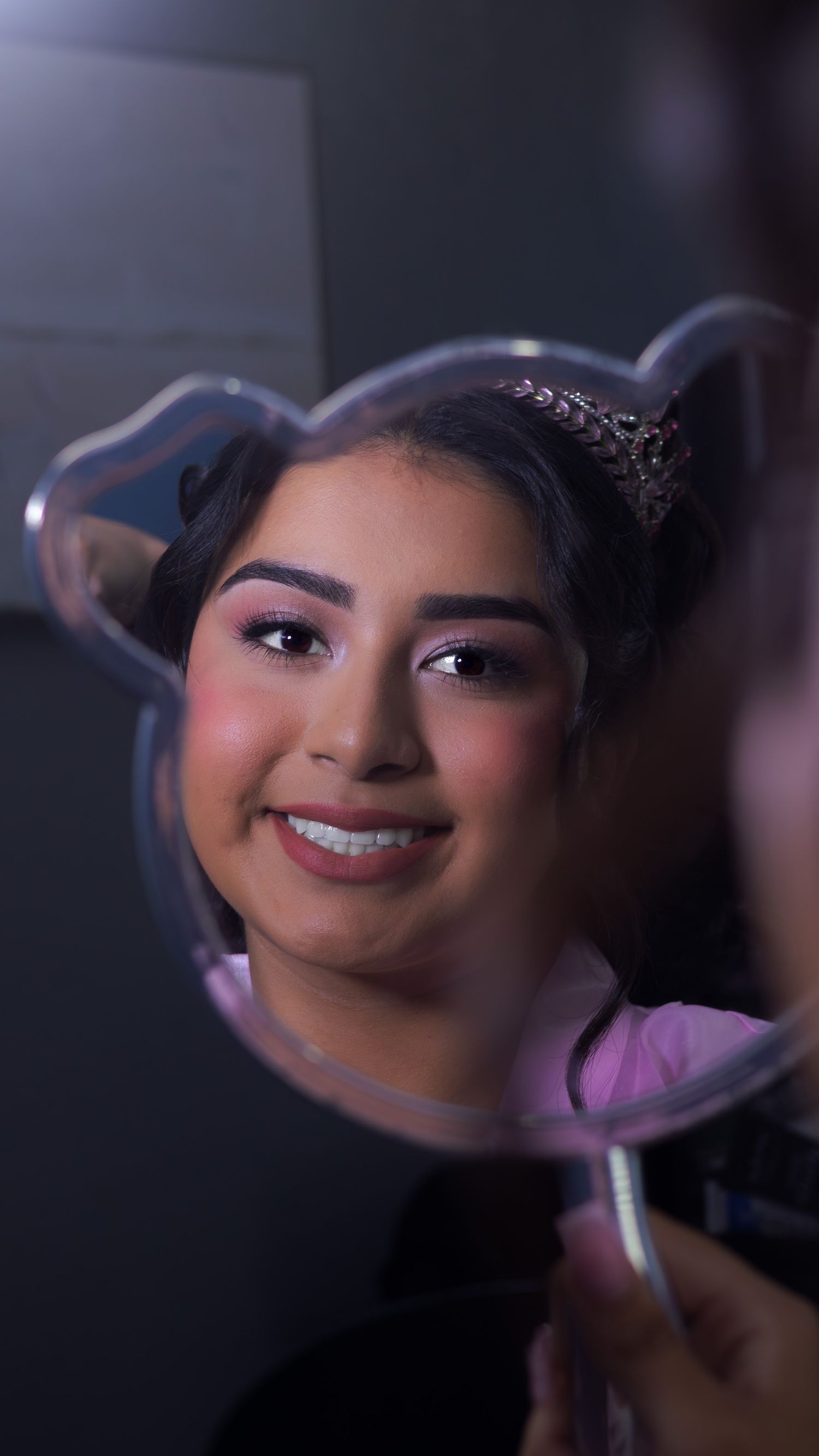 Reflections in a handheld mirror showing glamorous makeup and styling details. At a Quinceañera