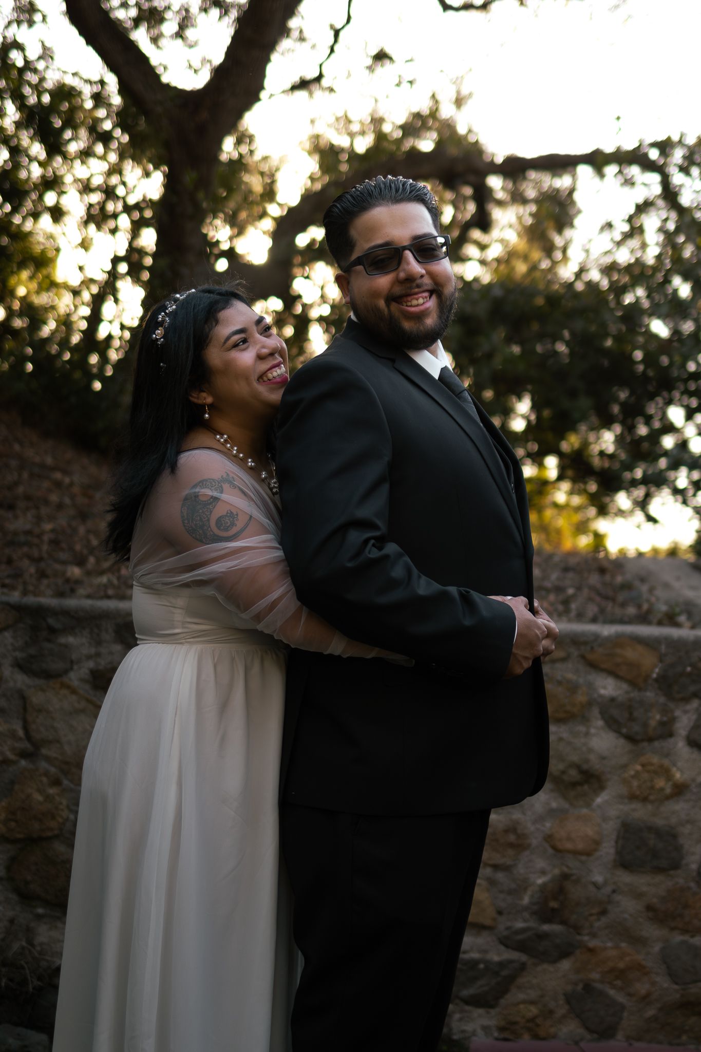 A couple shares a joyful moment at sunset, with the bride in a flowing white dress and groom in classic black suit.