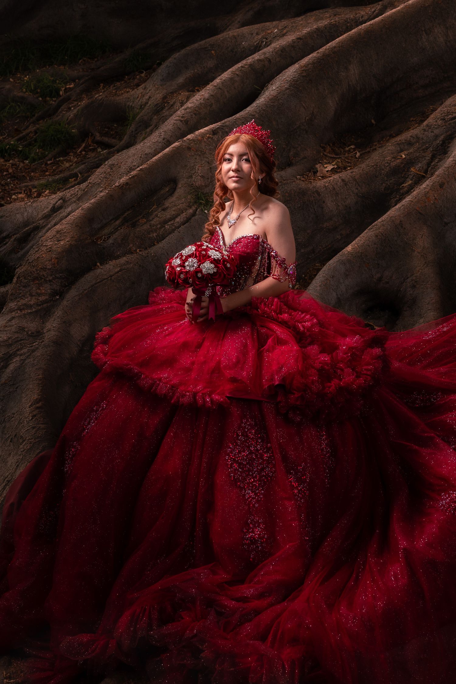 Flowing crimson gown with tulle layers spreads across rugged terrain in an ethereal fashion photograph.
