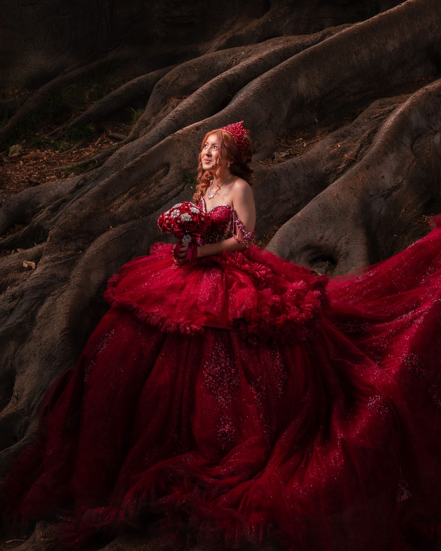 A flowing red gown with intricate details cascades over dark rocks in a dramatic fashion photography scene.