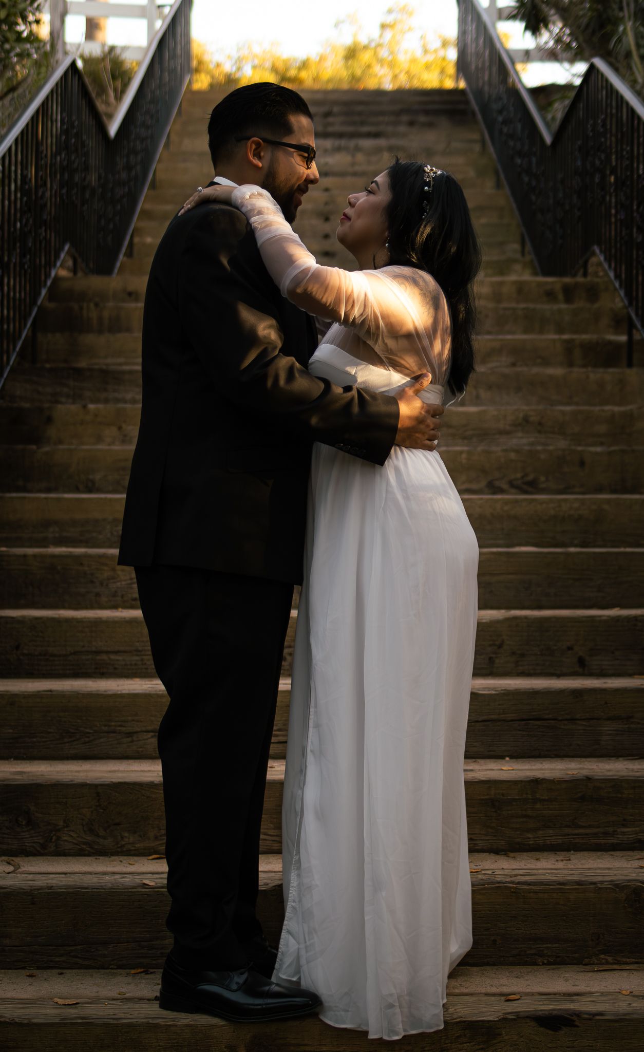 A romantic couple embraces on stone steps during a wedding photoshoot at sunset.