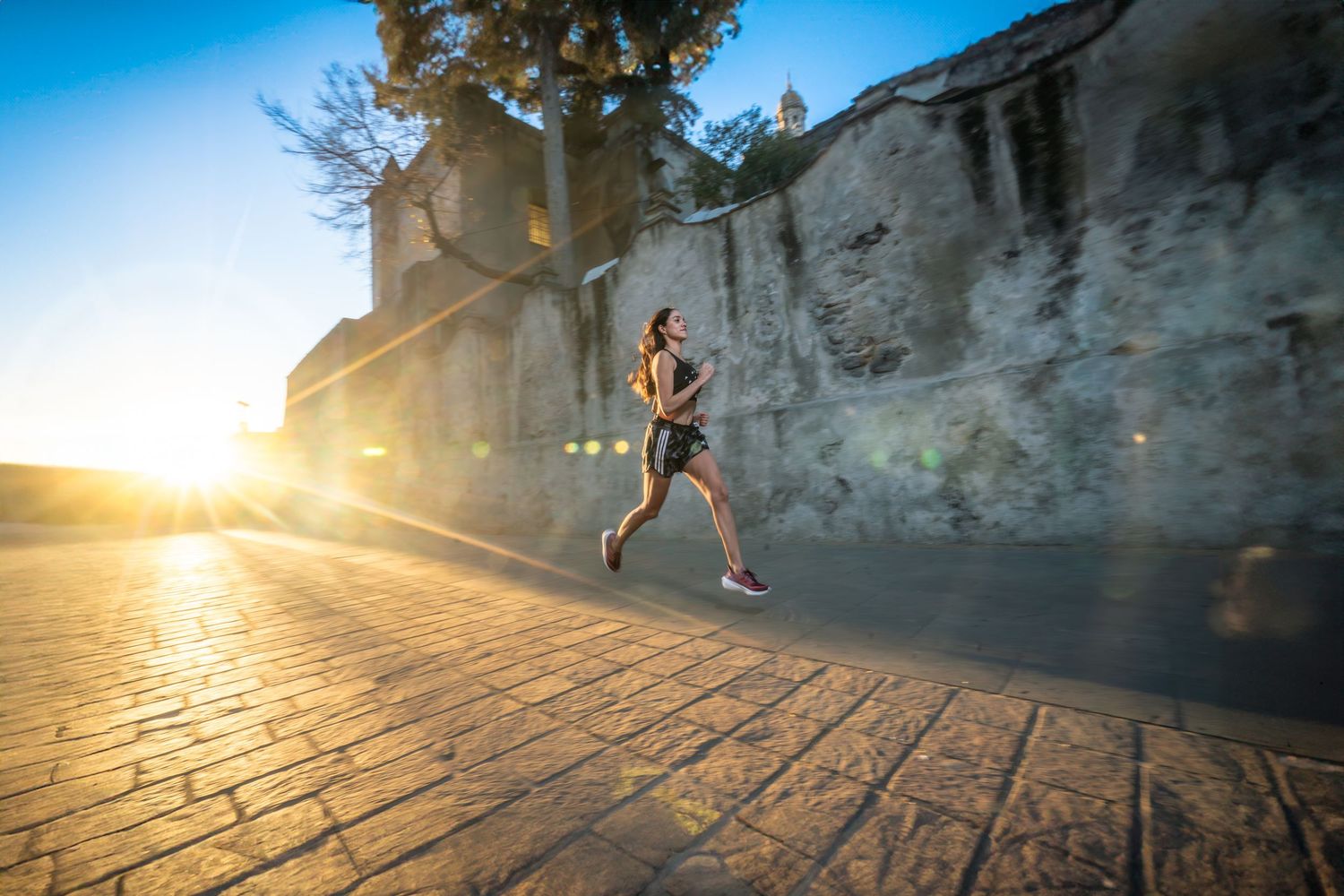 Person jumping on cobblestone street at sunset with dramatic lens flare.
