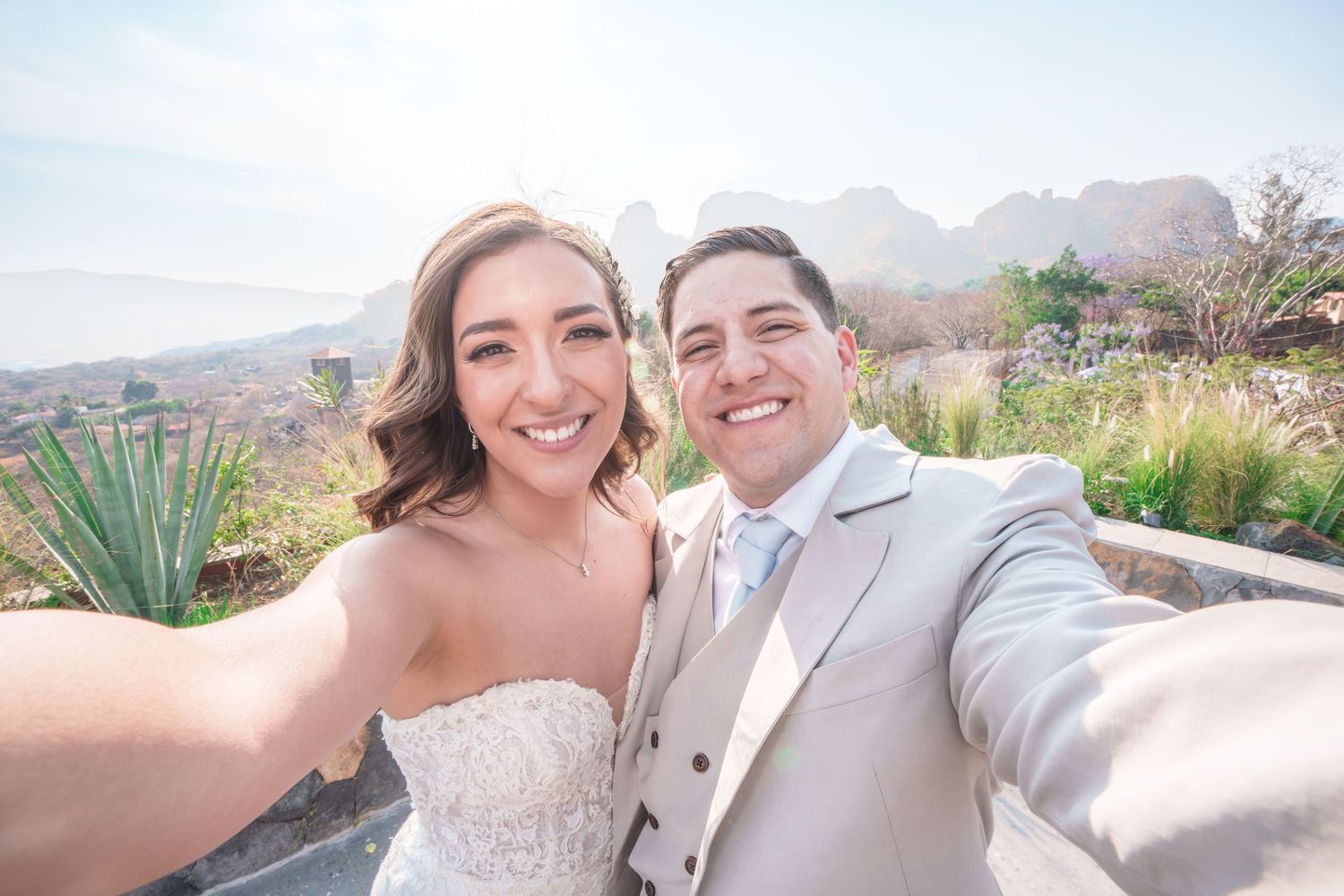 A couple takes a selfie together outdoors with mountains and desert landscape visible in the background.