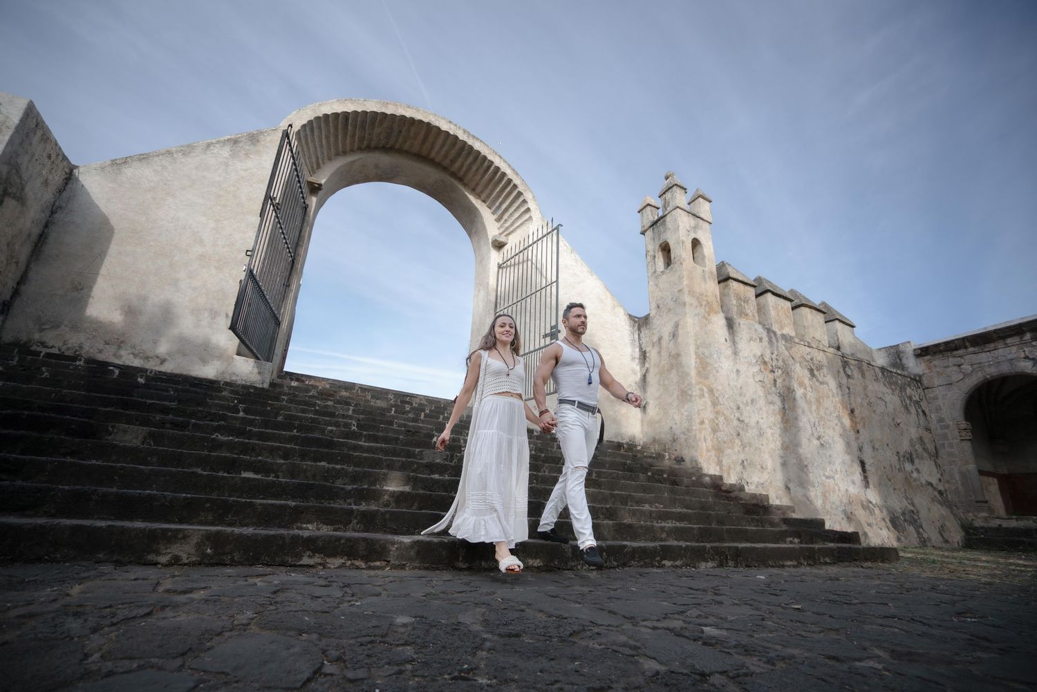 A couple descends stone steps at a historic church archway during a destination photoshoot. Fotografía artística de bodas | CDMX y destino
