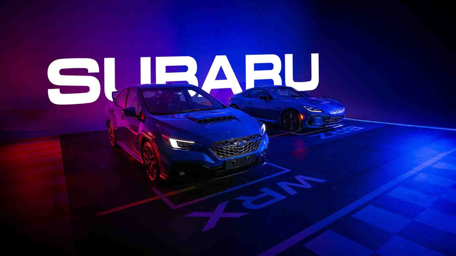 Subaru vehicles displayed under dramatic blue and purple lighting at auto show.